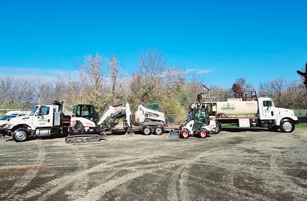 A row of construction vehicles are parked in a dirt lot.