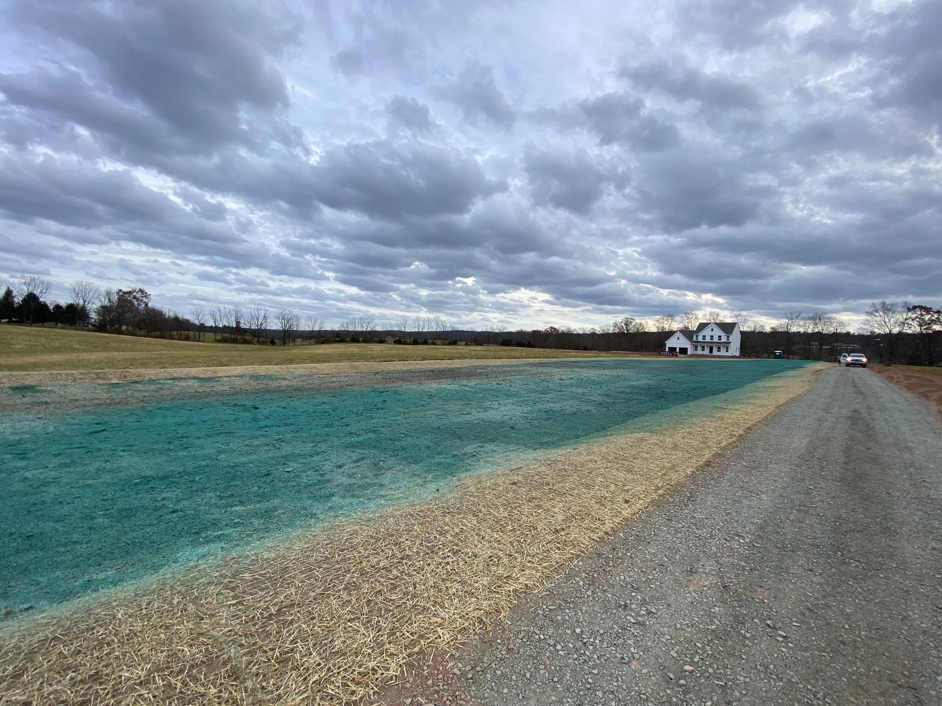 A dirt road going through a field with a house in the background.