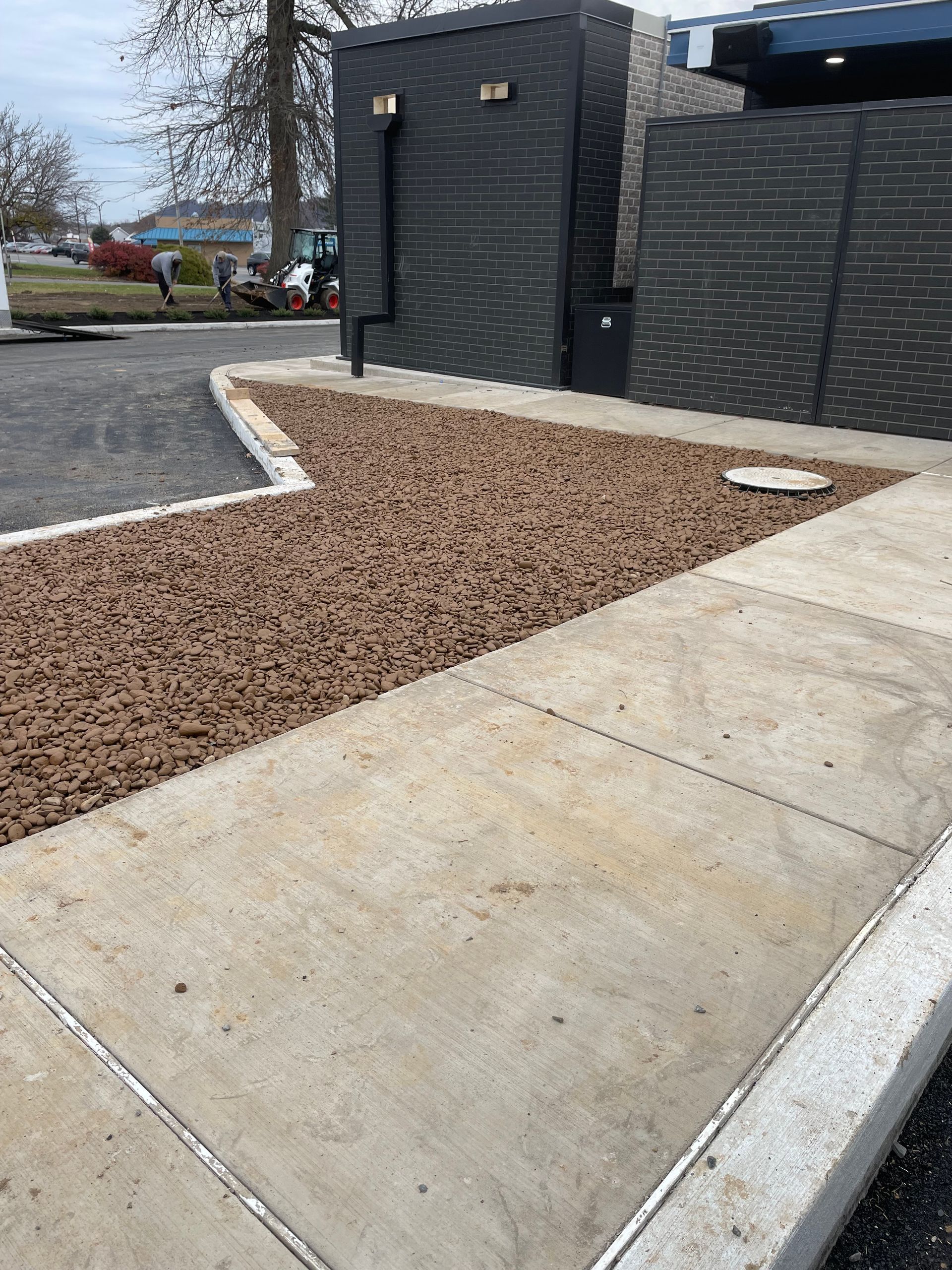 Construction site: Bobcat excavator and worker digging in field of straw, viewed through car mirror.