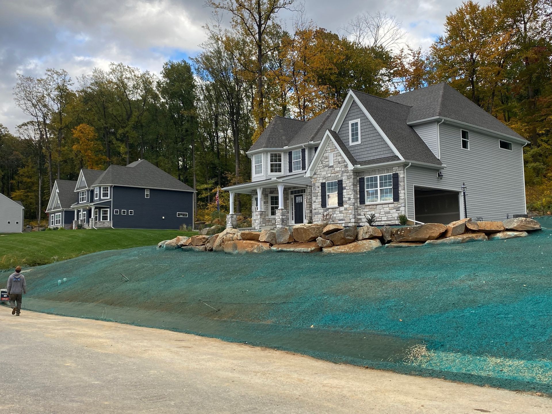 A man is walking towards a house on a hill with hydroseeding installed by complete property solutions of Lancaster PA