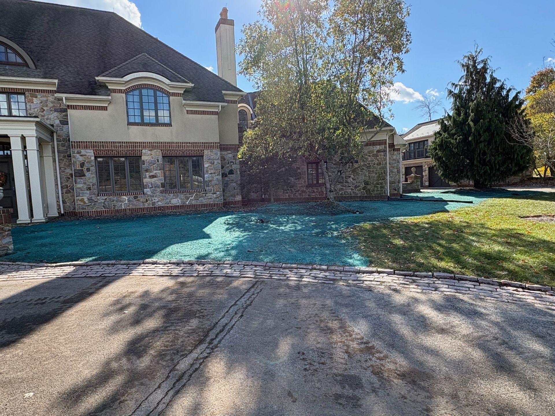 Large house with stone and brick facade; newly seeded lawn; sunny day.