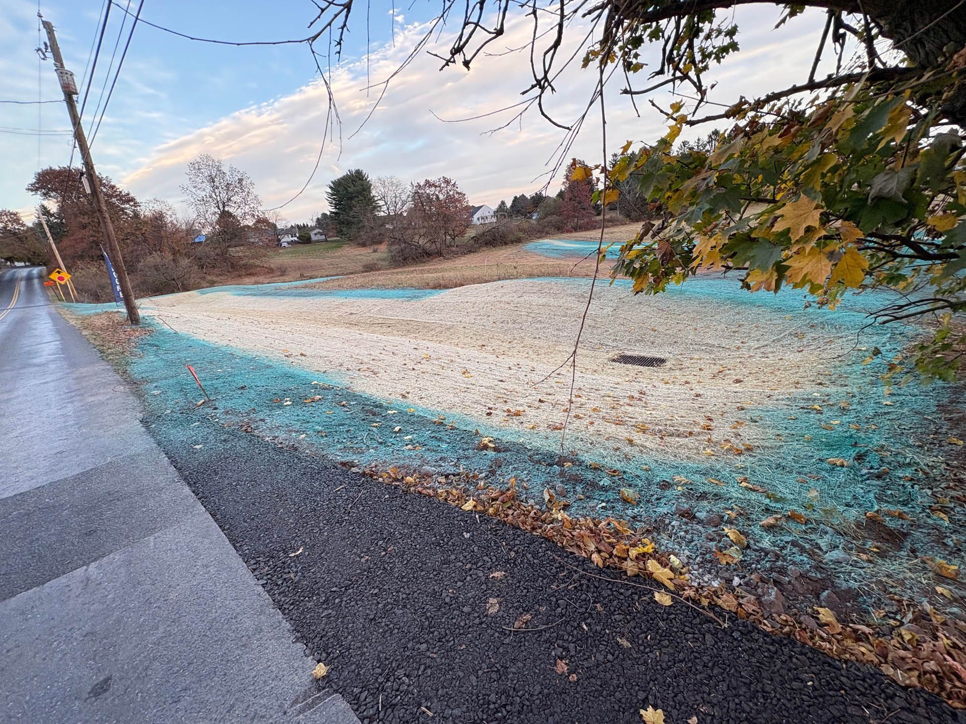 A large pile of tan material sits in a field with construction vehicles on top, cloudy sky.