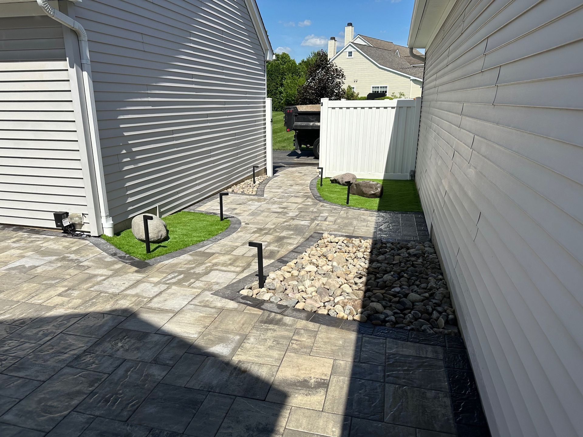 Stone pathway between two houses with grass, lights, and rocks.