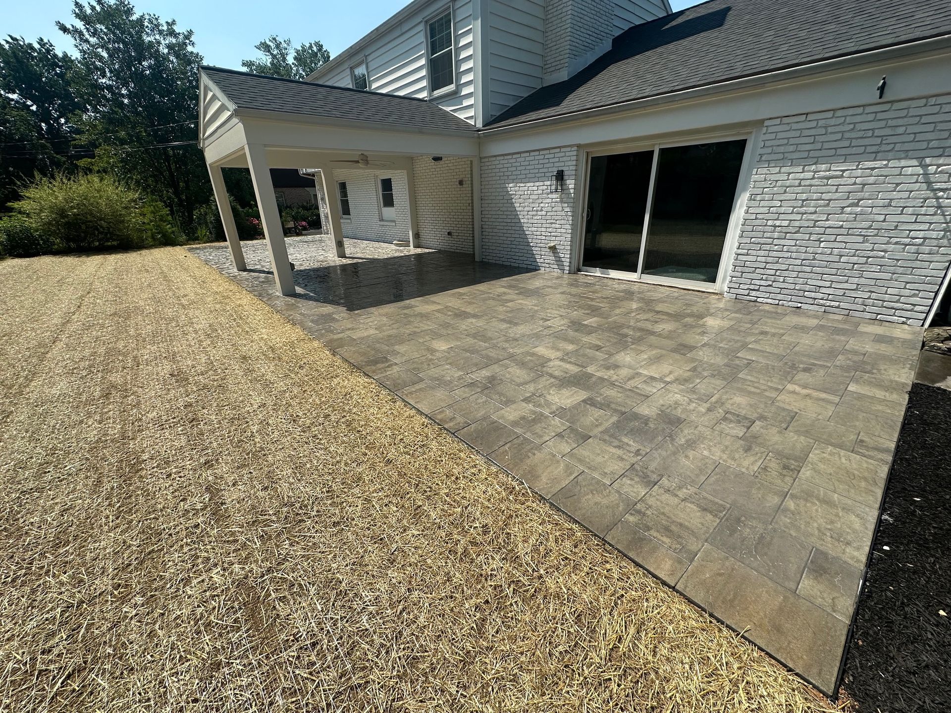 Brick patio next to house with covered porch. Gravel on the left, sliding glass door.
