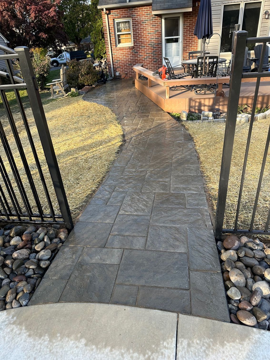 Stone walkway between black fences leads to a house with outdoor seating area.