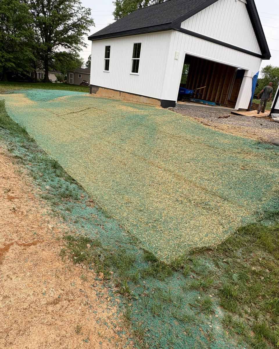 A newly seeded lawn covered with green netting, next to a white garage.