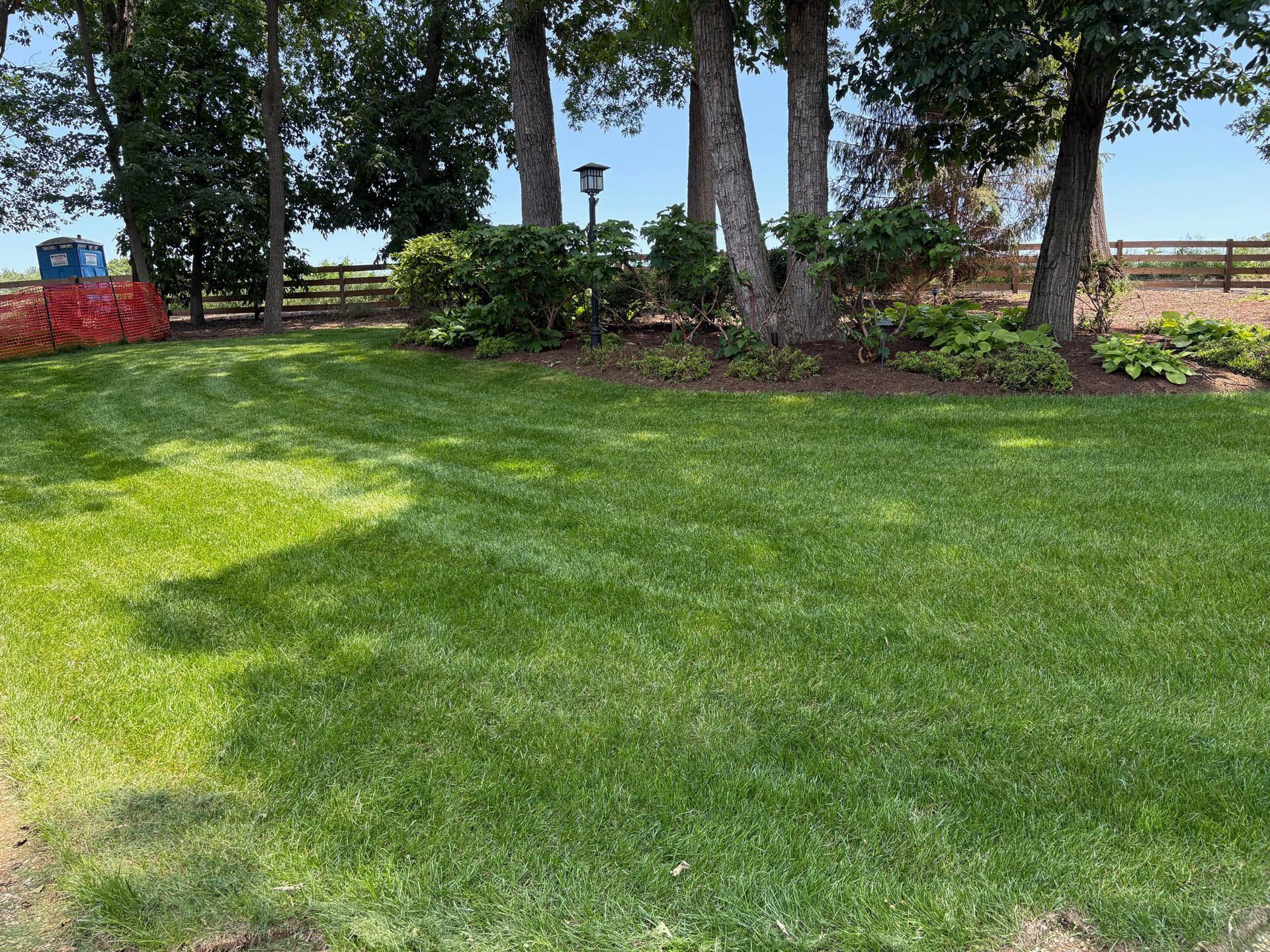 Lush green lawn with trees and shrubs in the background. A red barrier is in the left corner.