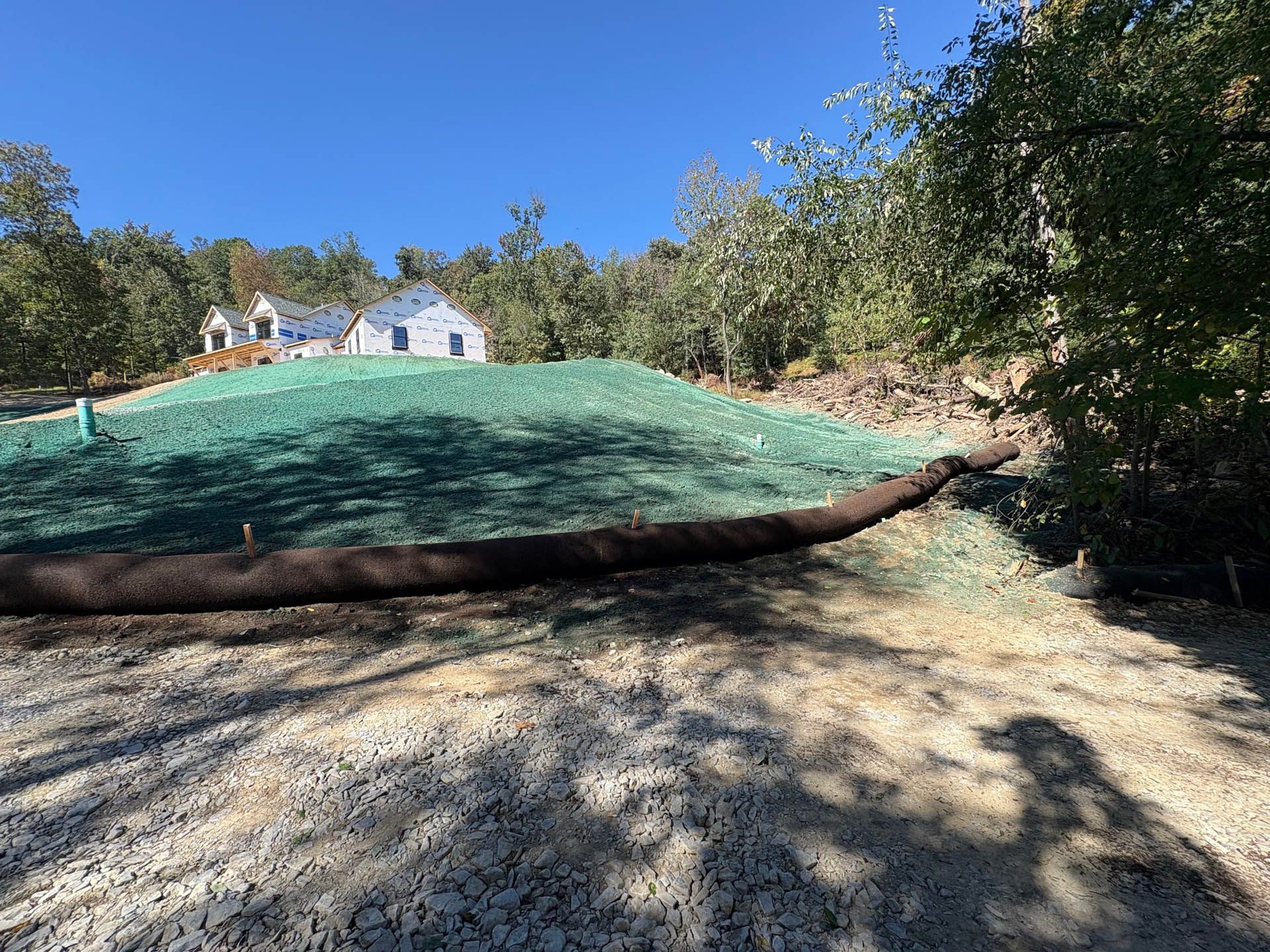 A hillside covered in green erosion control, gravel path, house in the distance, blue sky.
