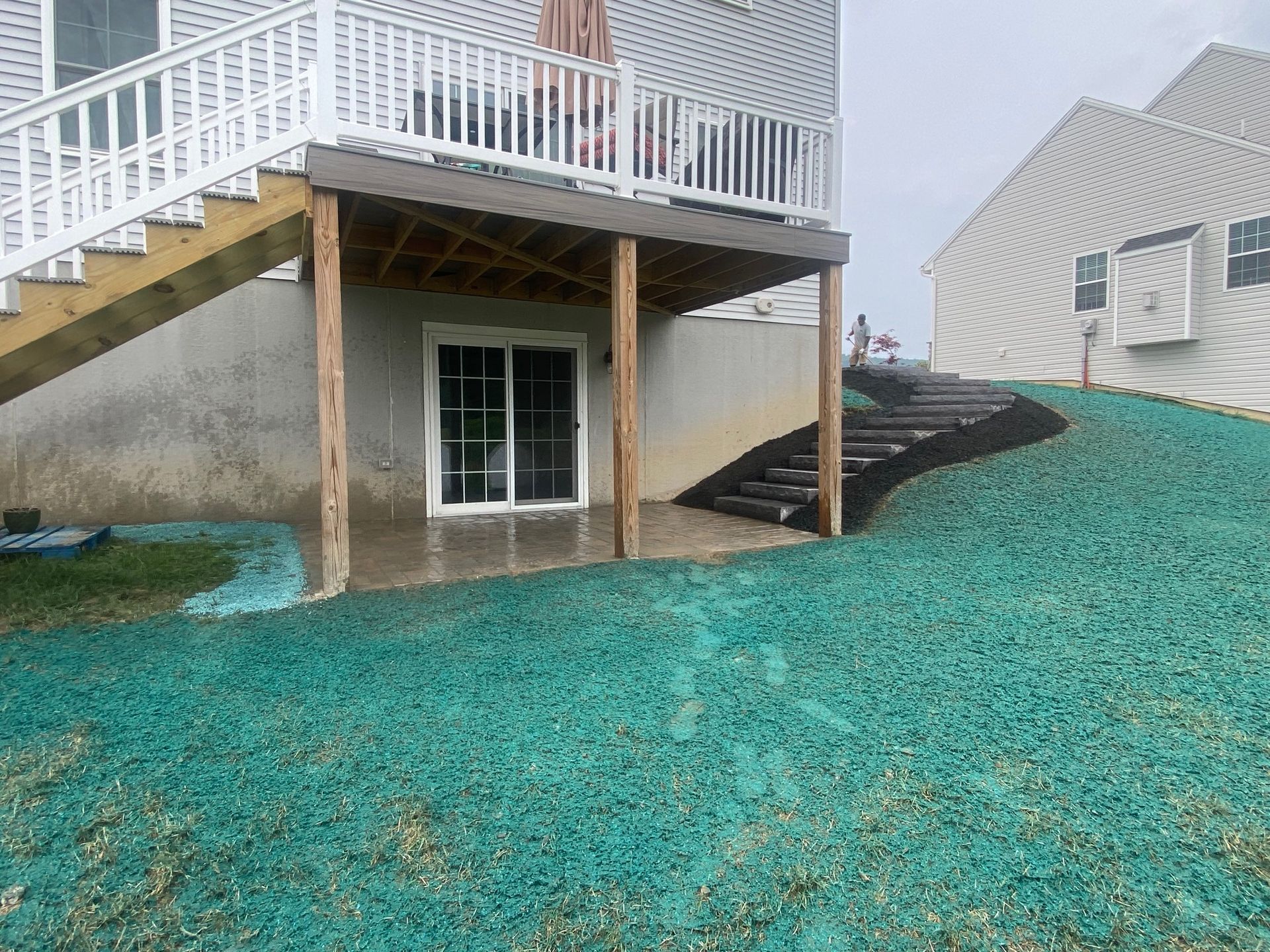 Backyard with deck, stairs, sliding door. Green gravel ground cover, dark mulch border.