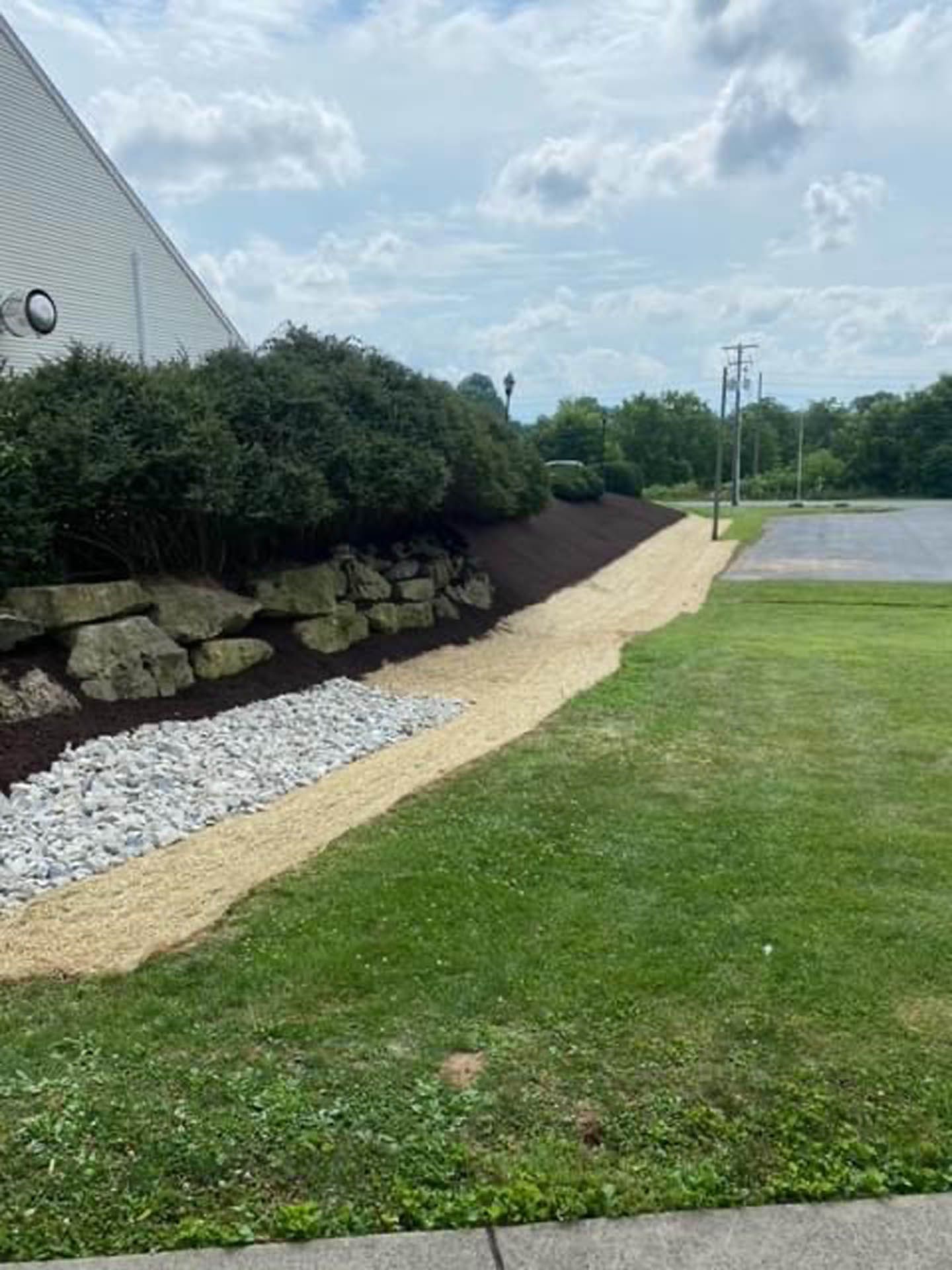 Stone retaining wall with a path of tan gravel and green grass next to a building.