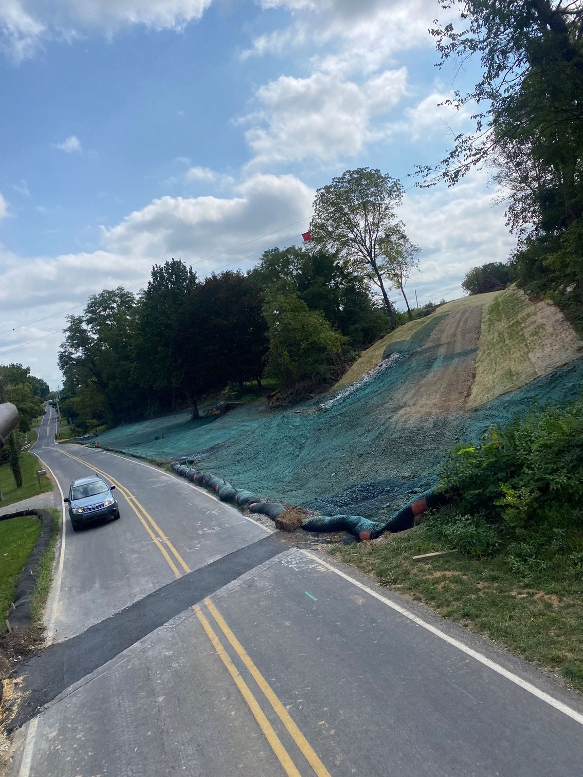 A car is driving down a road next to a hill.