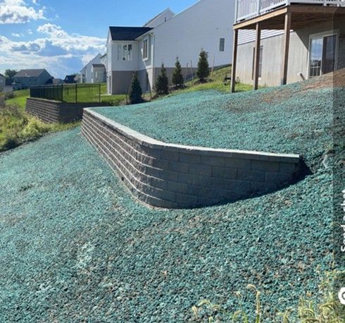 Curved retaining wall made of gray bricks on a grassy hillside, with houses in the background.