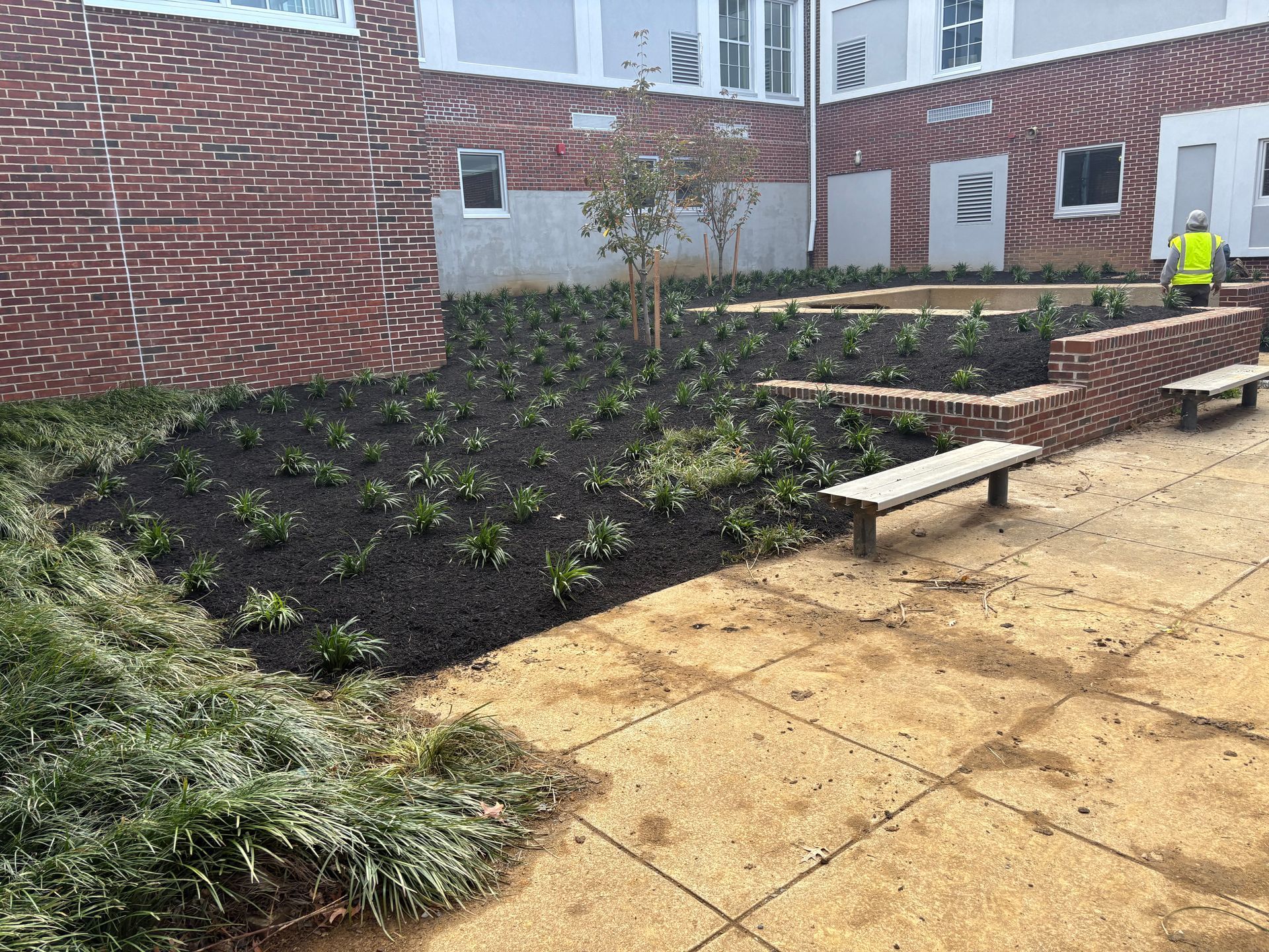 Courtyard with brick planters, benches, and landscaping. A worker in a vest is visible.
