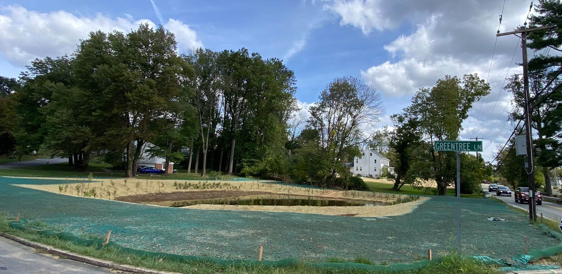 A grassy area with trees and a sign. A blue sky with clouds.