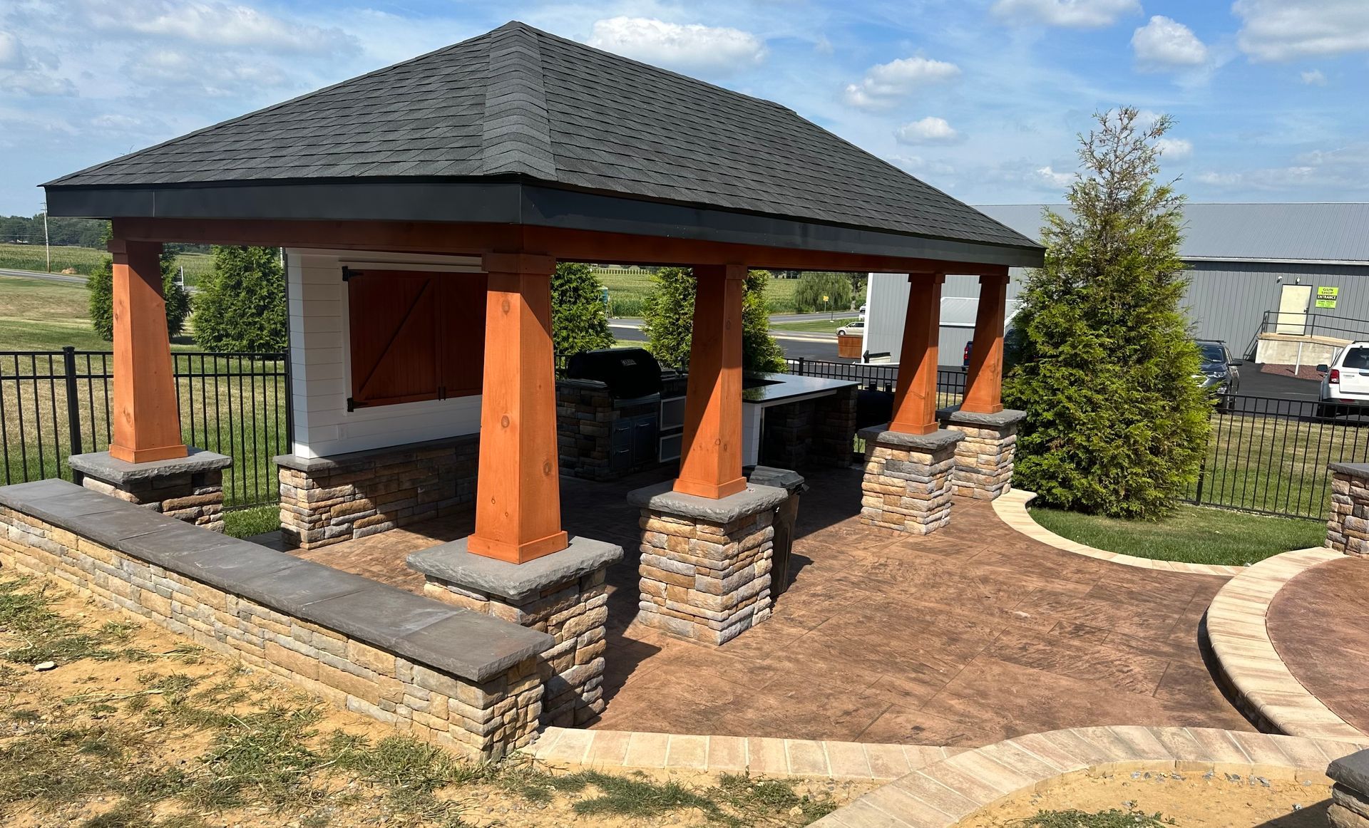 A wooden pavilion with a roof and pillars in a yard.