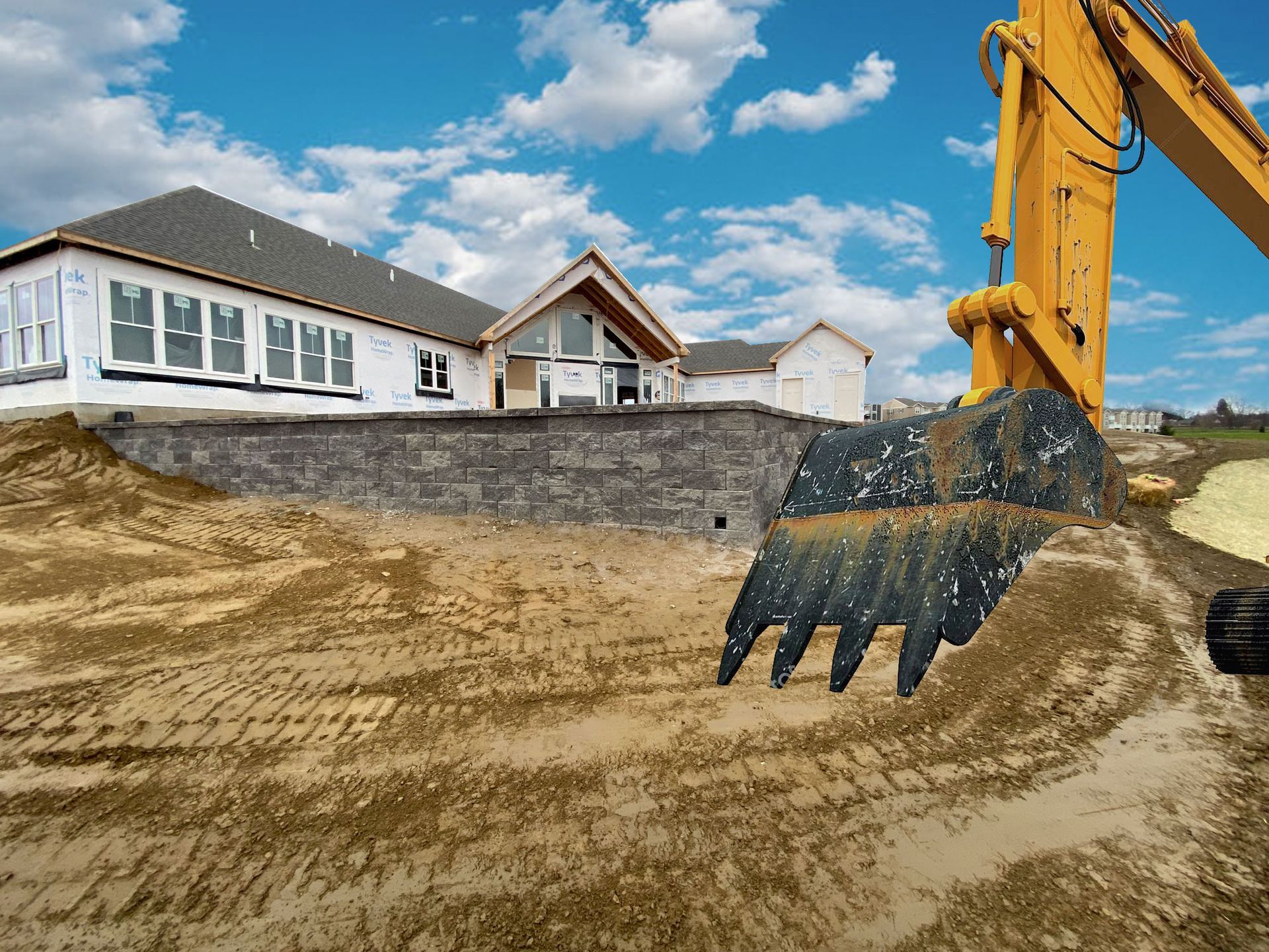 Construction site with an excavator moving dirt, a partially built building with windows in the background. Blue sky.
