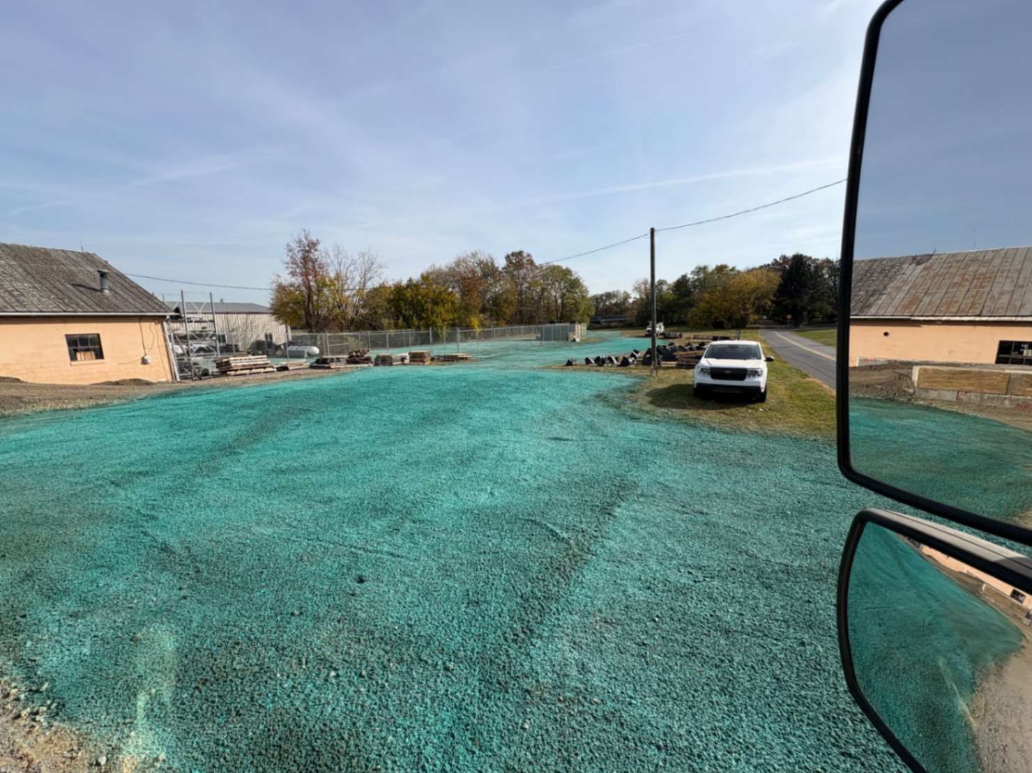 Green-covered land, likely seeded, with a vehicle and buildings. Rural setting, sunny day.