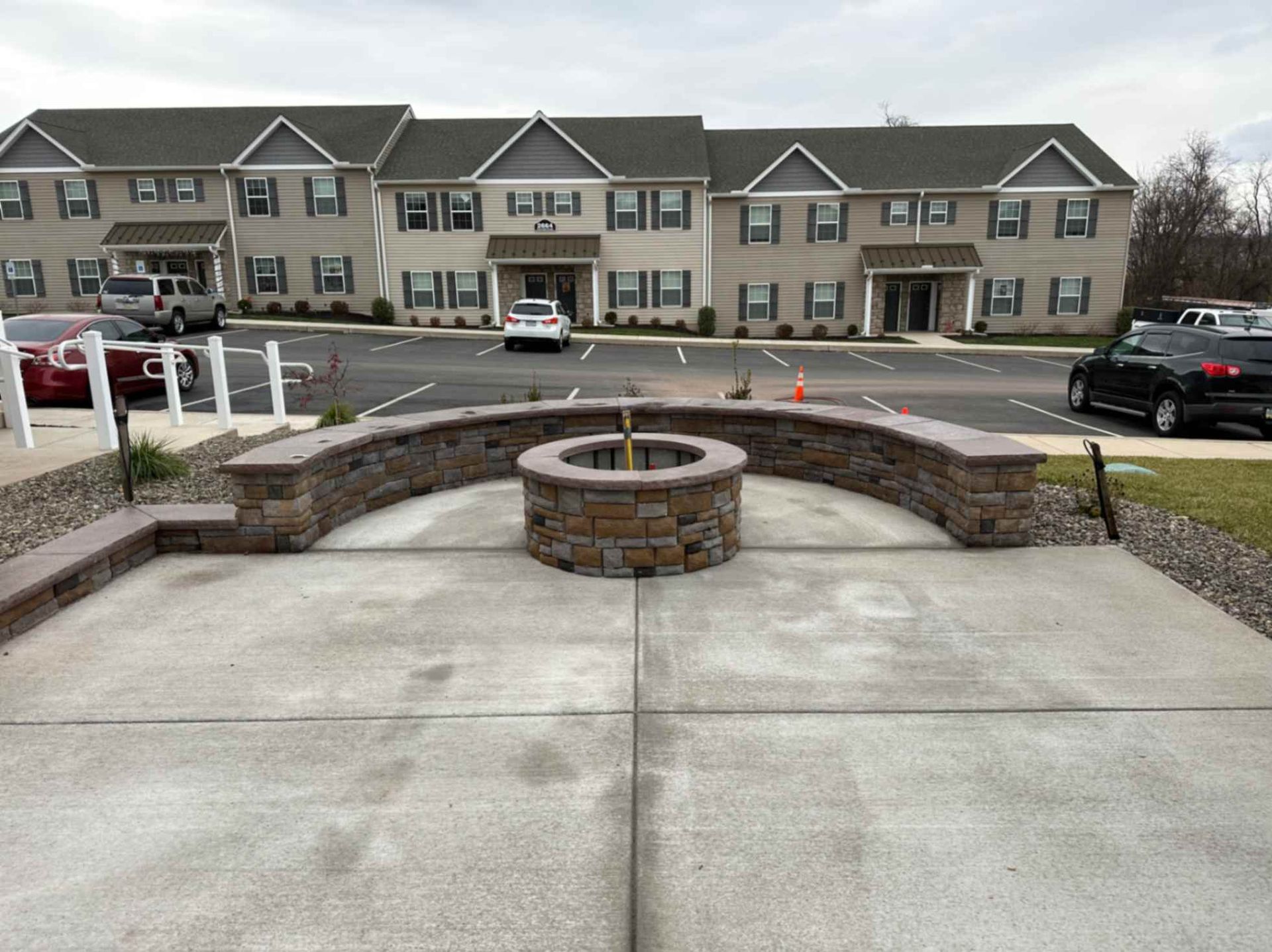 Concrete patio with a fire pit and curved stone seating, apartment building in background.