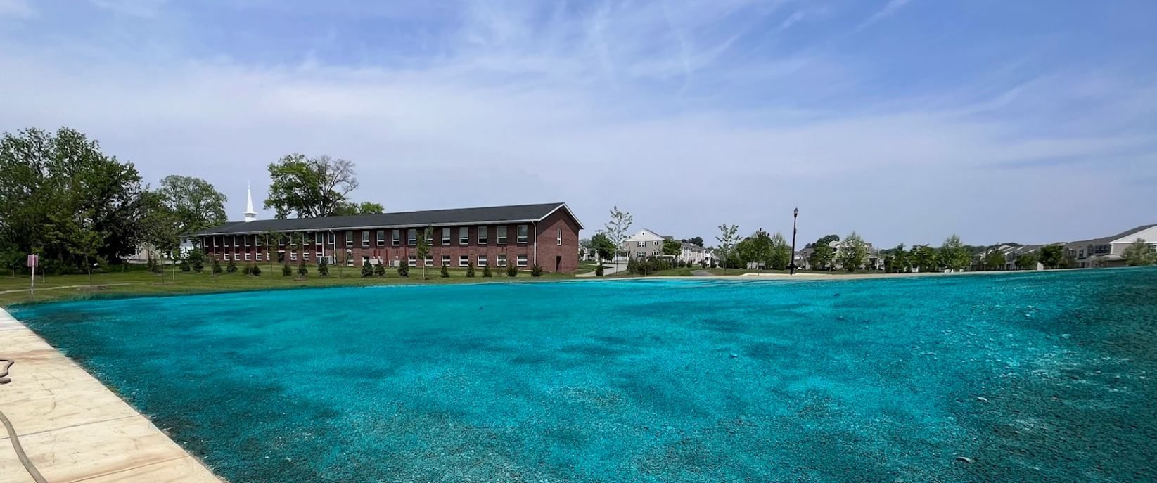 A long brick building sits beside turquoise water under a blue sky.