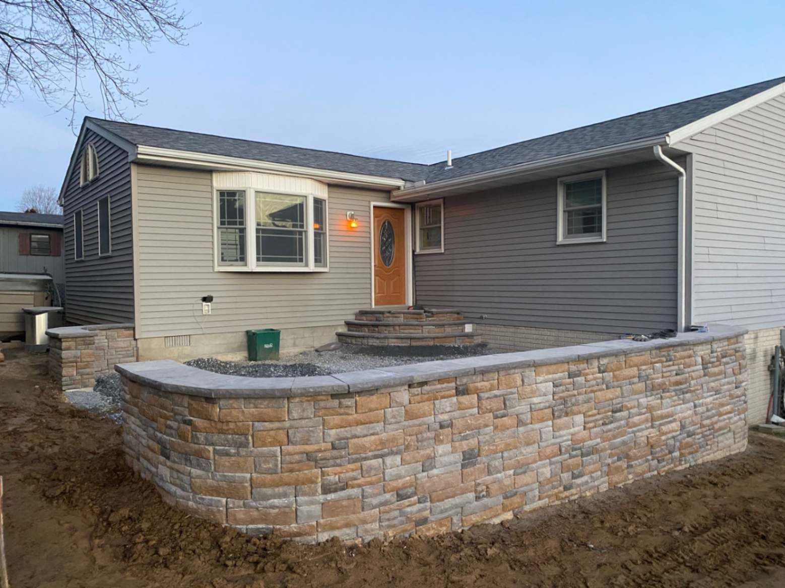 Home exterior with stacked stone retaining wall, front steps, and gray siding.
