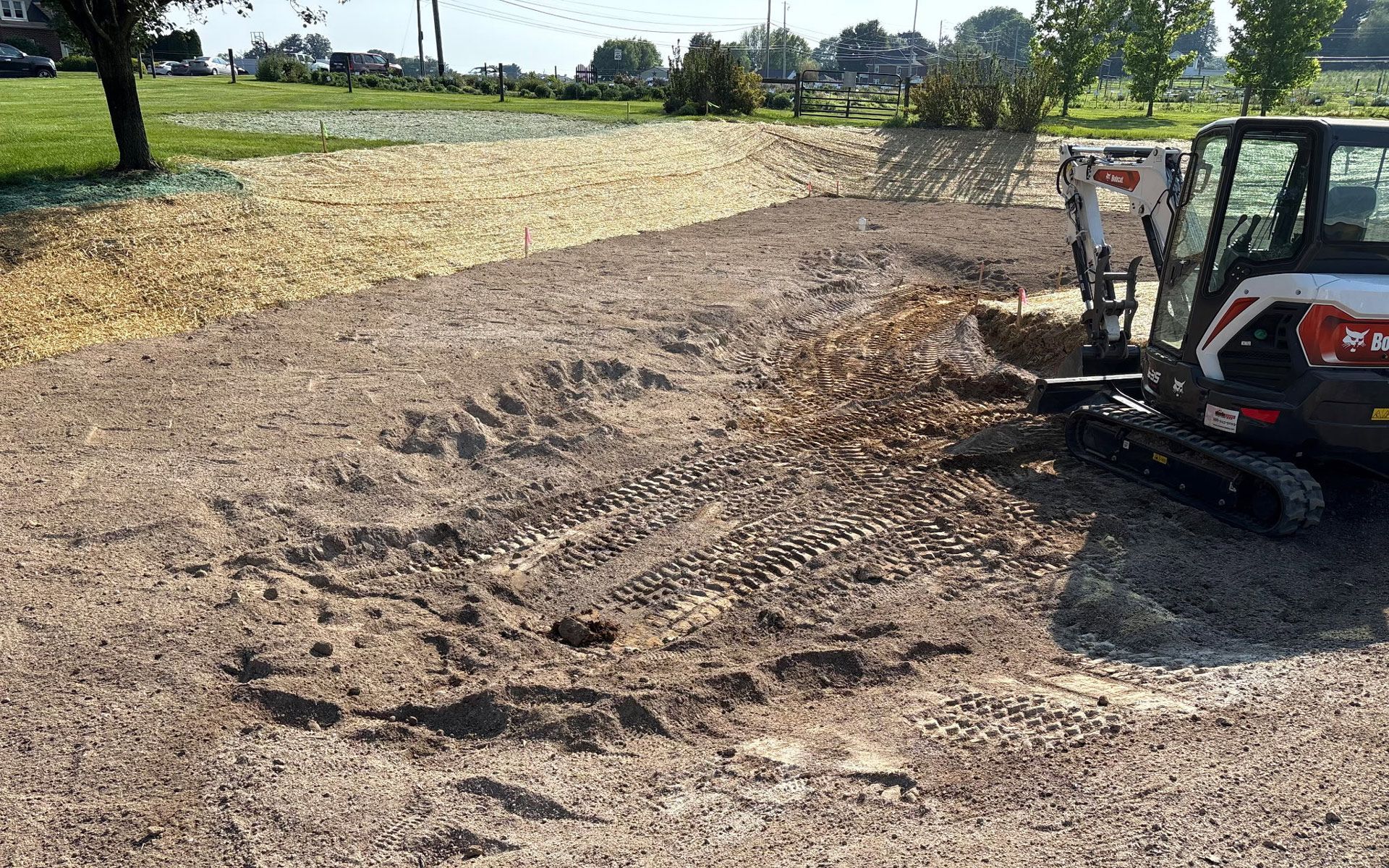 Construction site with an excavator moving dirt, a partially built building with windows in the background. Blue sky.