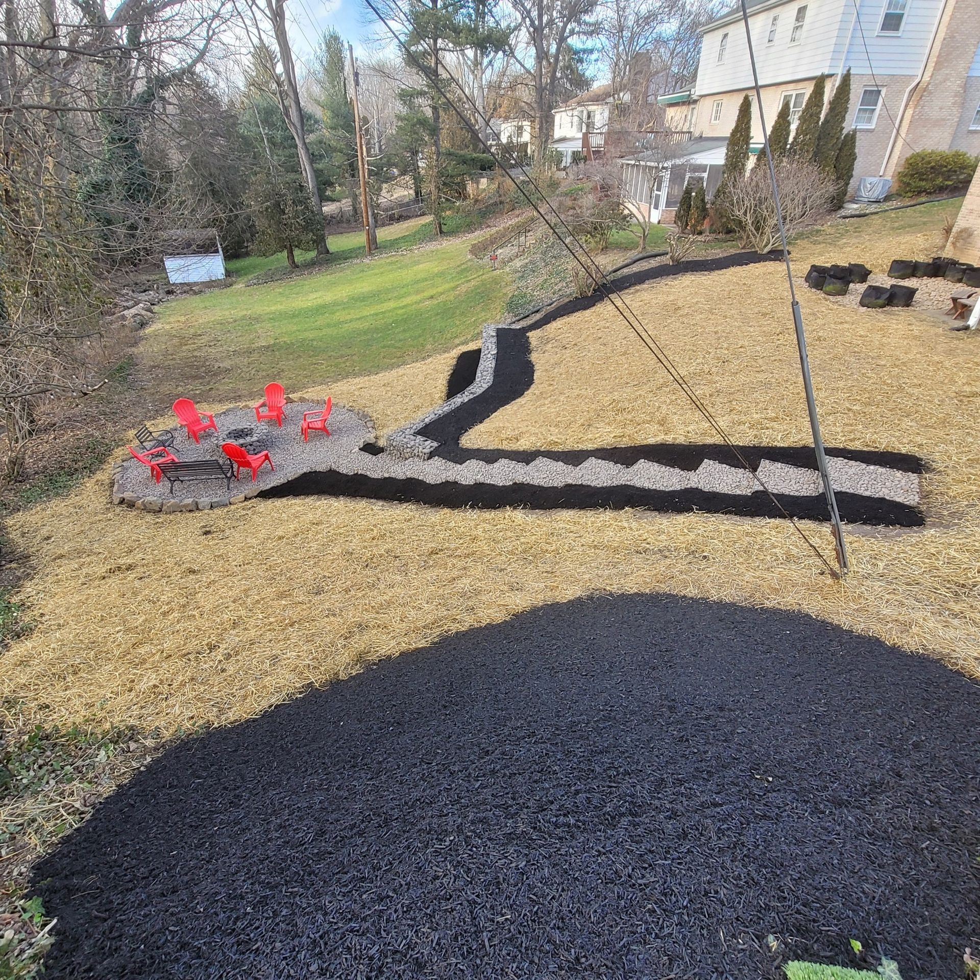 Backyard landscaping with fire pit, red chairs, gravel, and mulch.