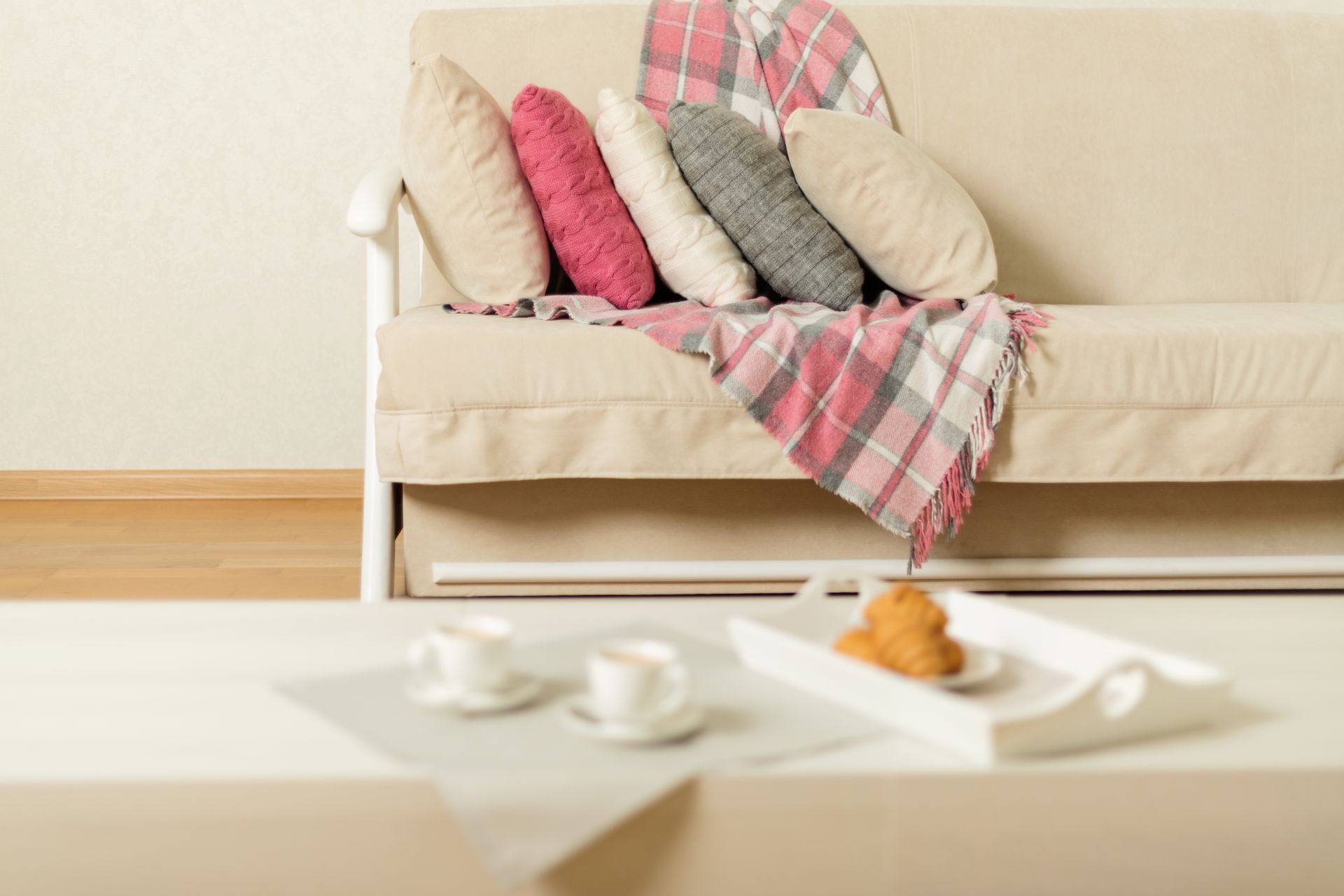 Beige futon with colorful pillows and a plaid blanket; coffee table with tray and cups.