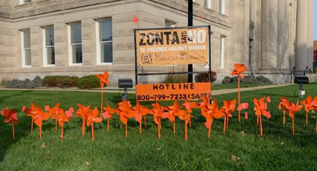 Orange pinwheels and sign on grass in front of a building; Zonta International logo, hotline number.