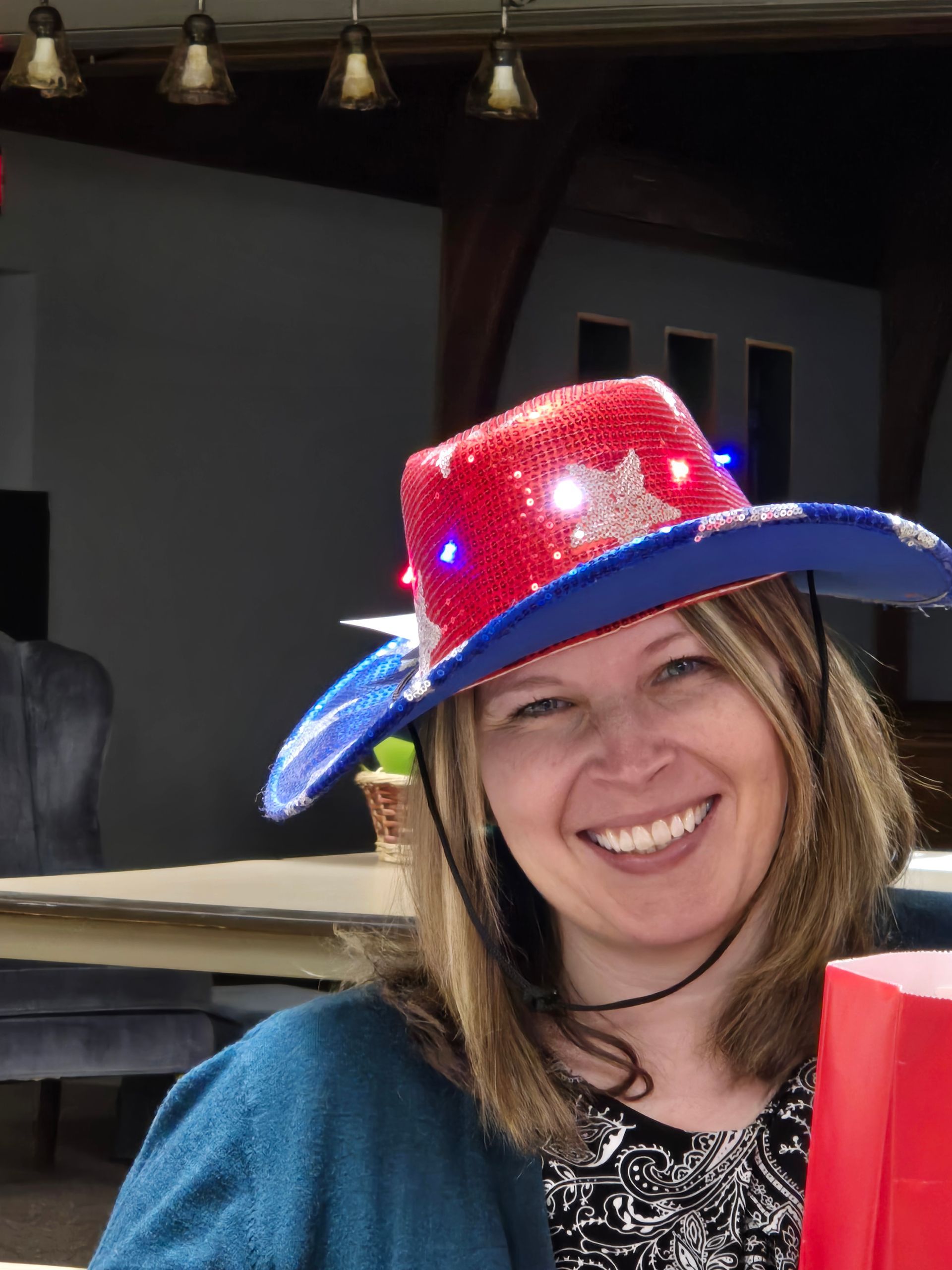 Woman smiling, wearing a red, white, and blue sequined cowboy hat with lights.