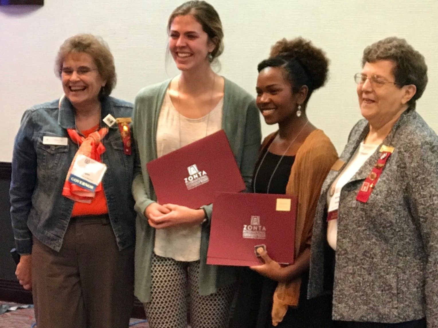 Four people smiling, holding certificates at an event.