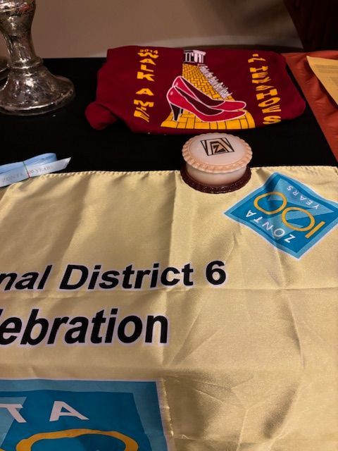Table with a banner, cosmetic compact, and a burgundy pouch, likely for a Zonta International District 6 Celebration.