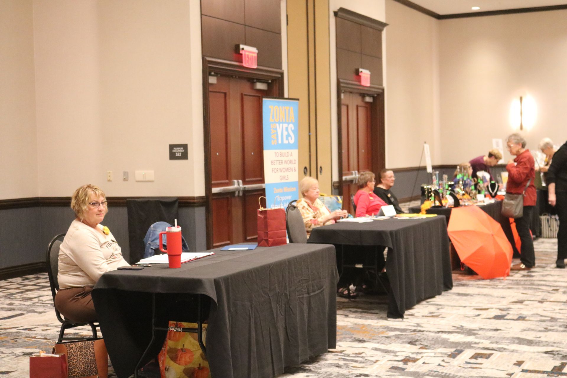 People seated at tables with black tablecloths in a conference room. Display with 
