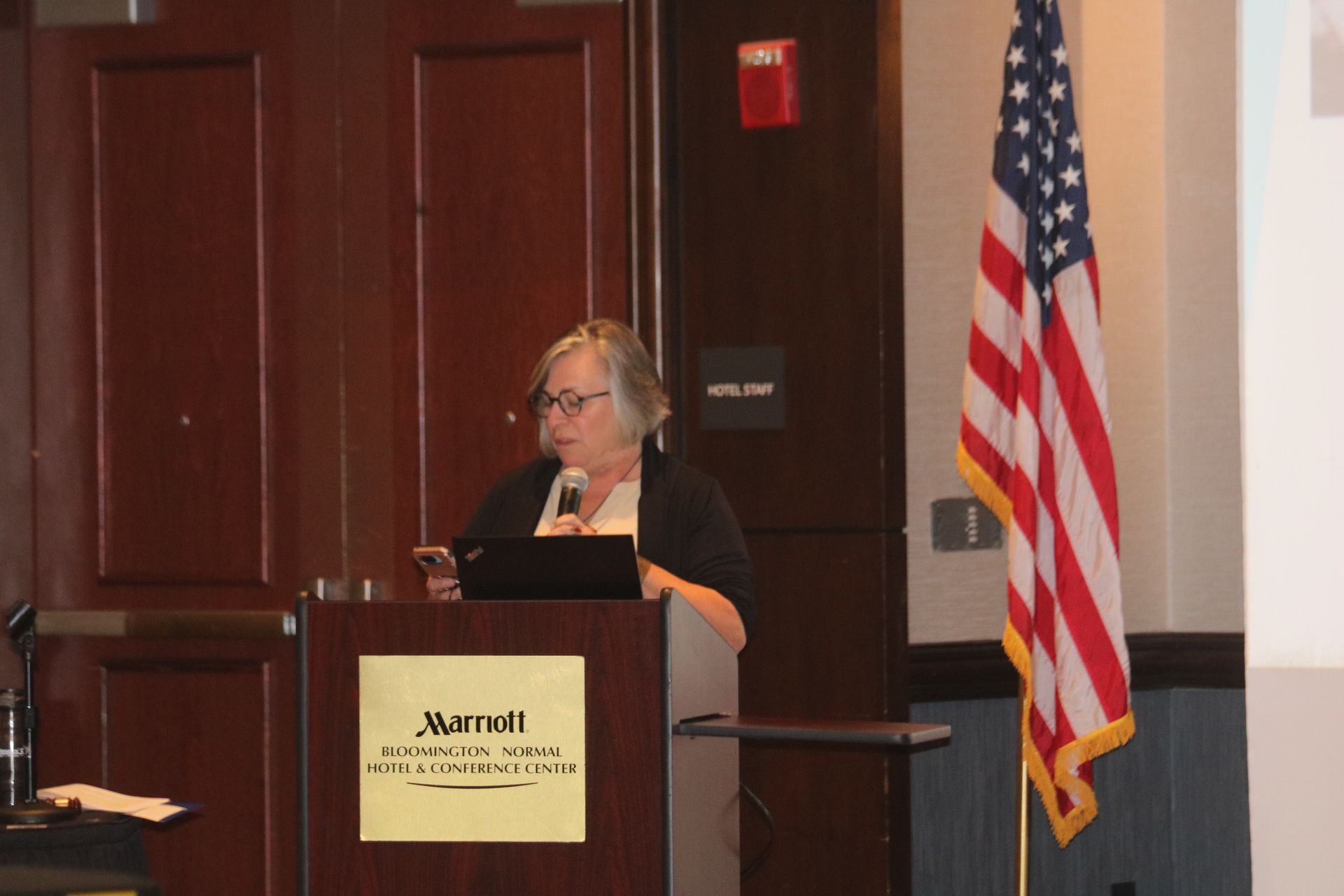 Woman speaking at a Marriott podium with an American flag to the right.