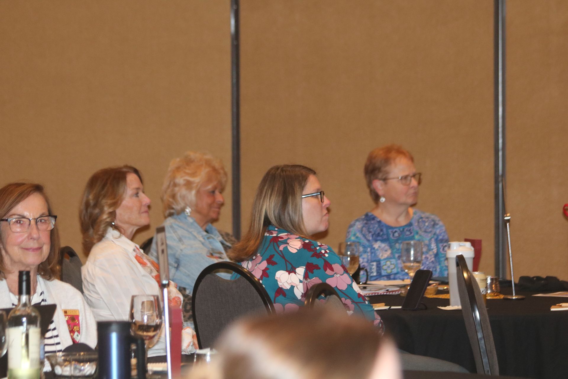 People seated at a conference table, listening attentively. Some have glasses and wear casual clothing.