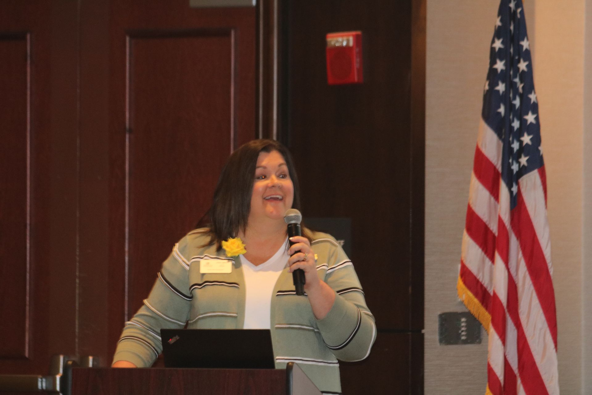 Woman speaking at a podium with microphone, American flag in background.