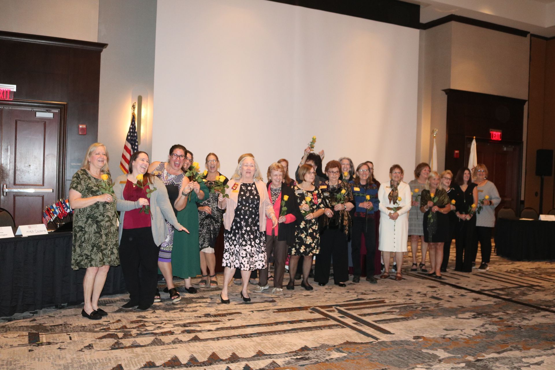 Group of women holding flowers standing in a room with an American flag.