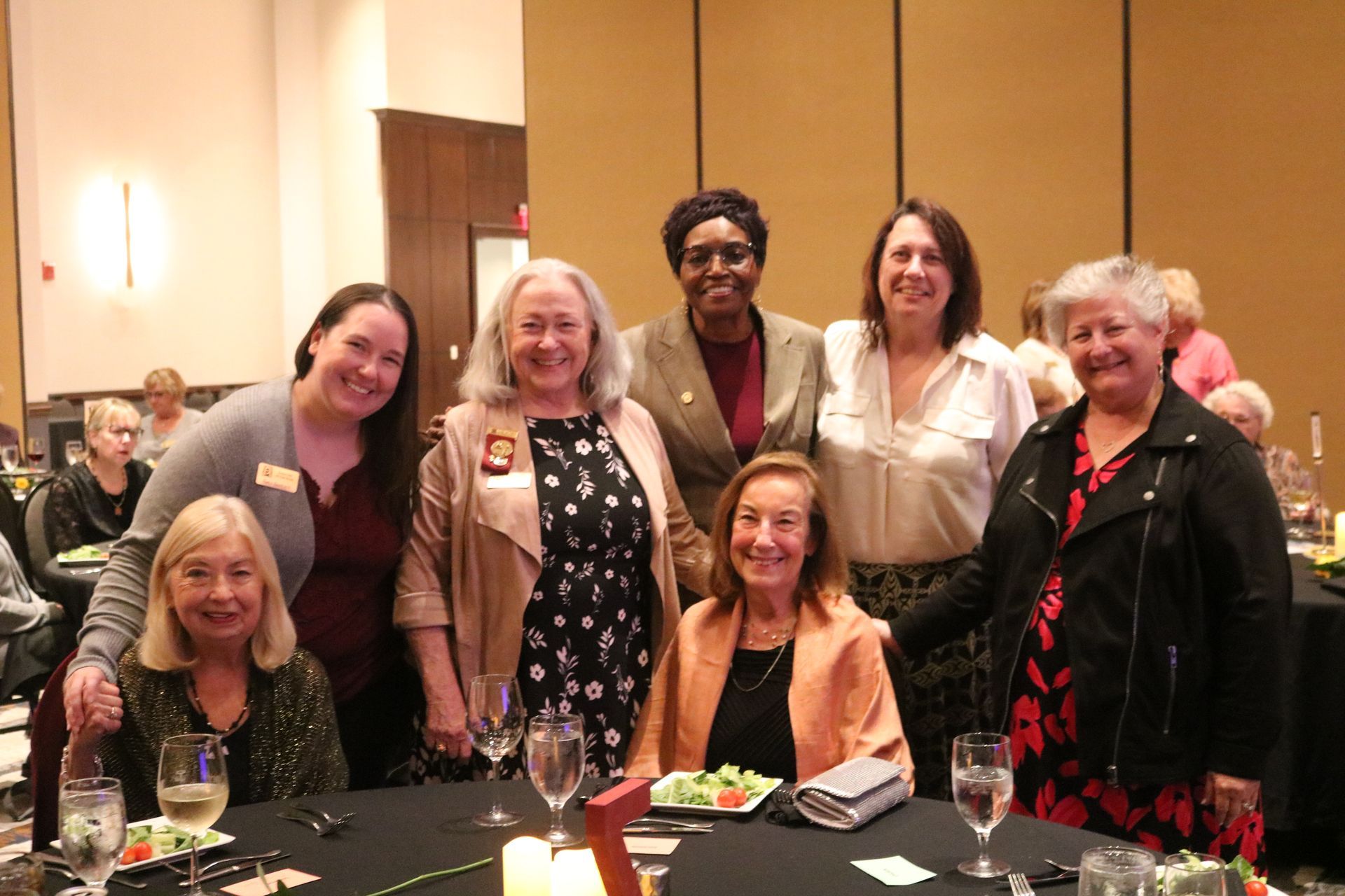 Group of women posing together at a table in a well-lit banquet hall.