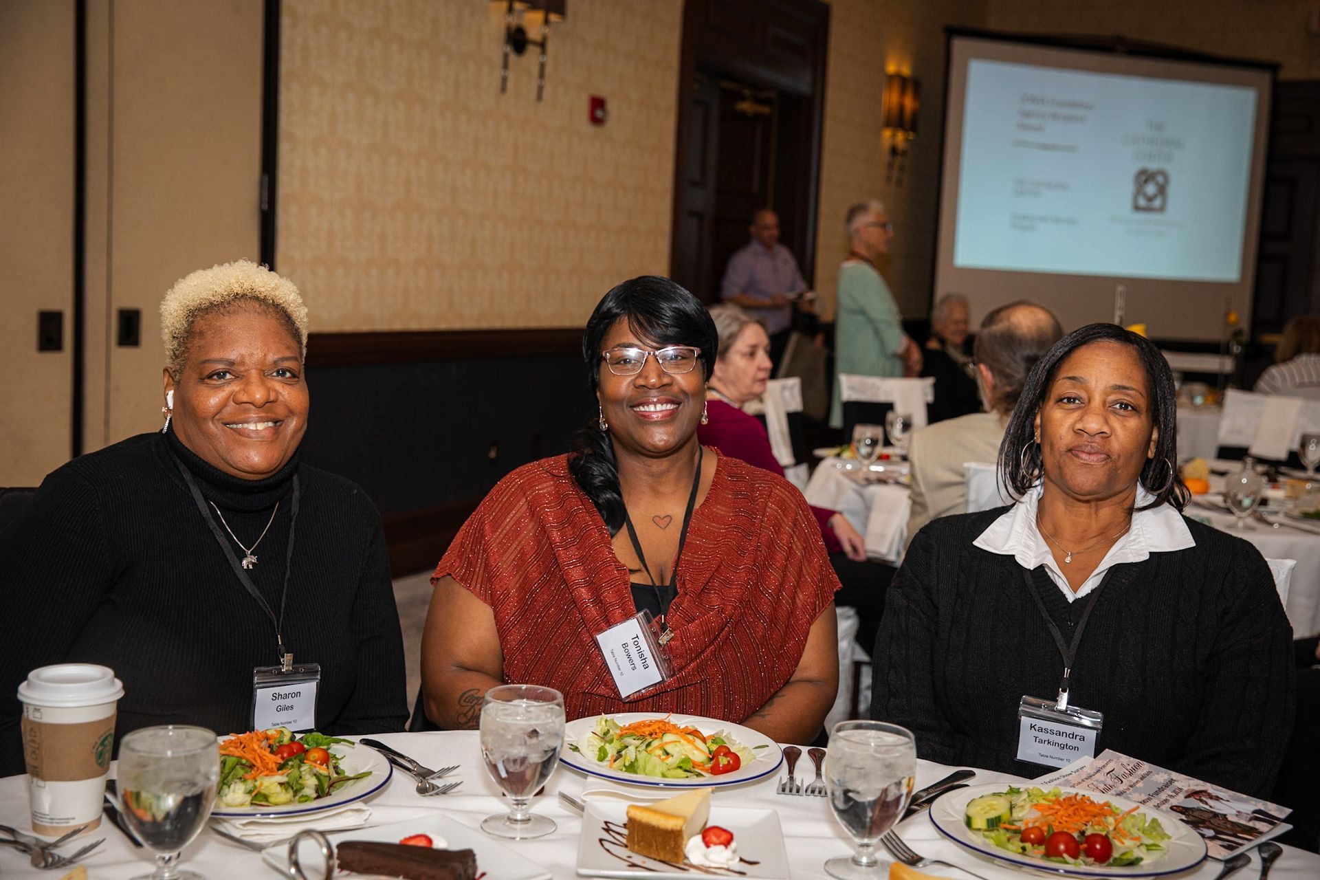 Three women seated at a table in a conference room, smiling. Salad plates and water glasses in front of them.