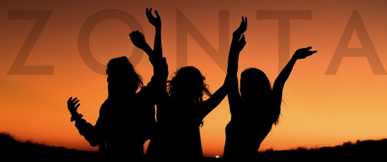 Silhouetted figures of three women with arms raised against a fiery sunset background. The word