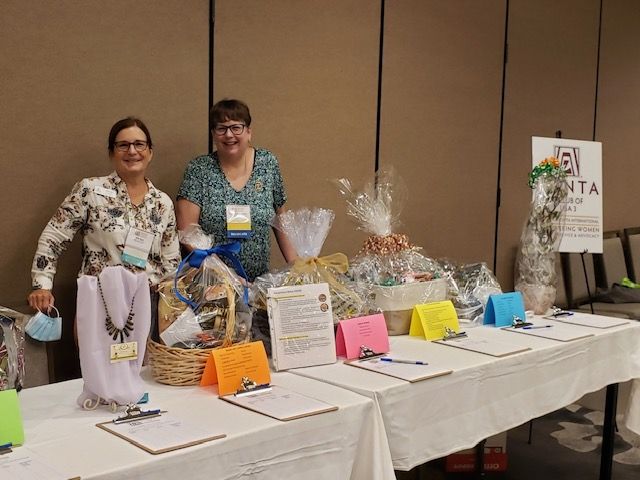 Two women at a fundraising table with gift baskets and bid sheets at an event.