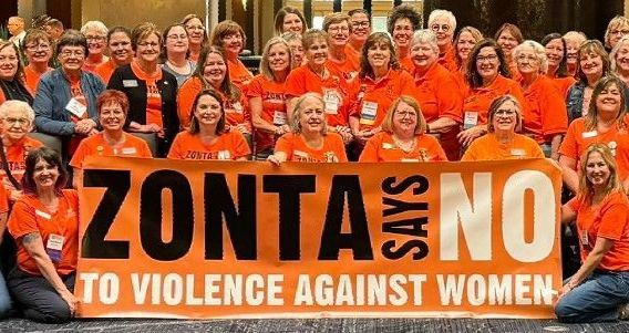 Group of women in orange shirts holding a banner that says