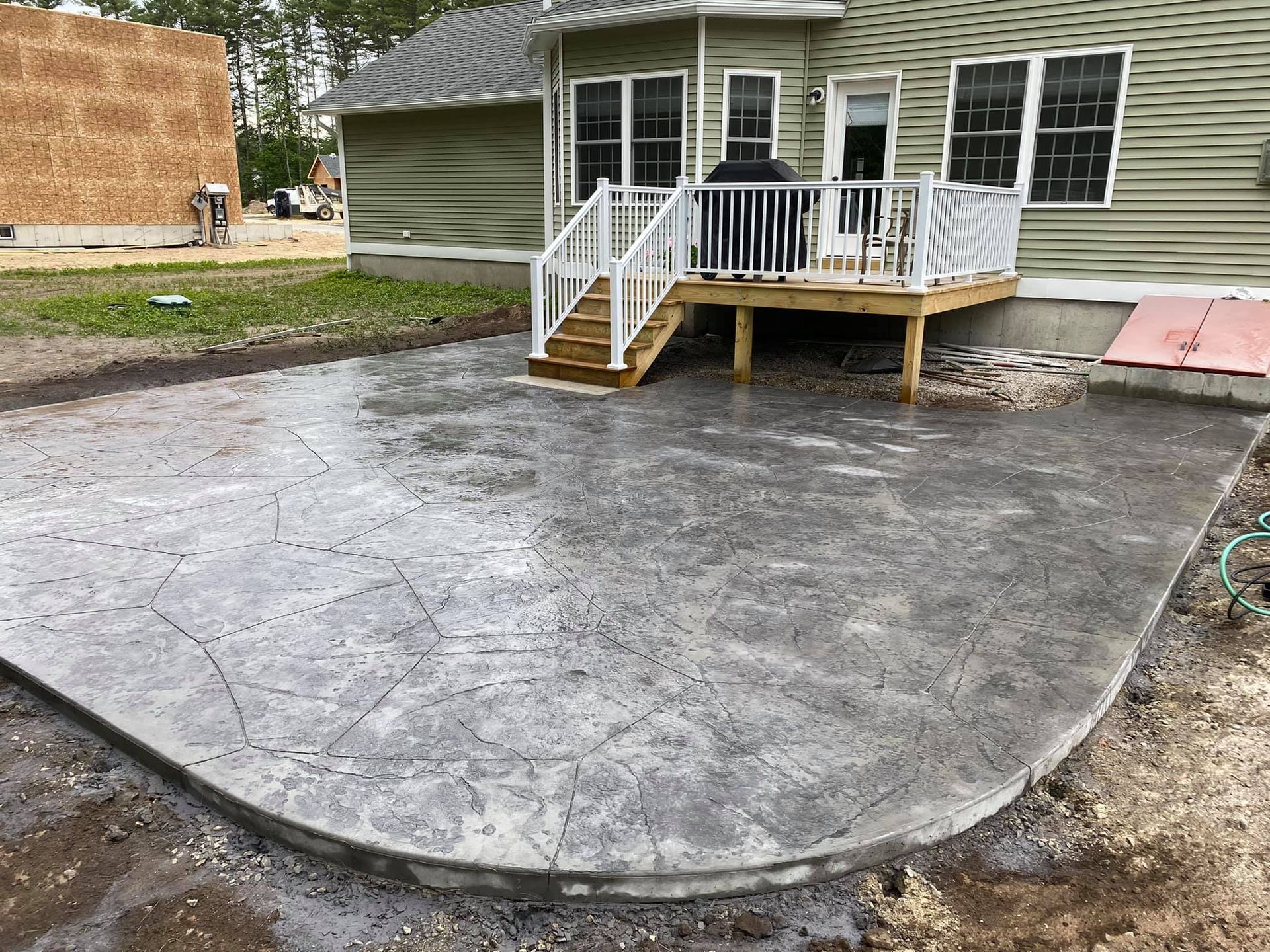 A concrete patio with a deck and stairs in front of a house.