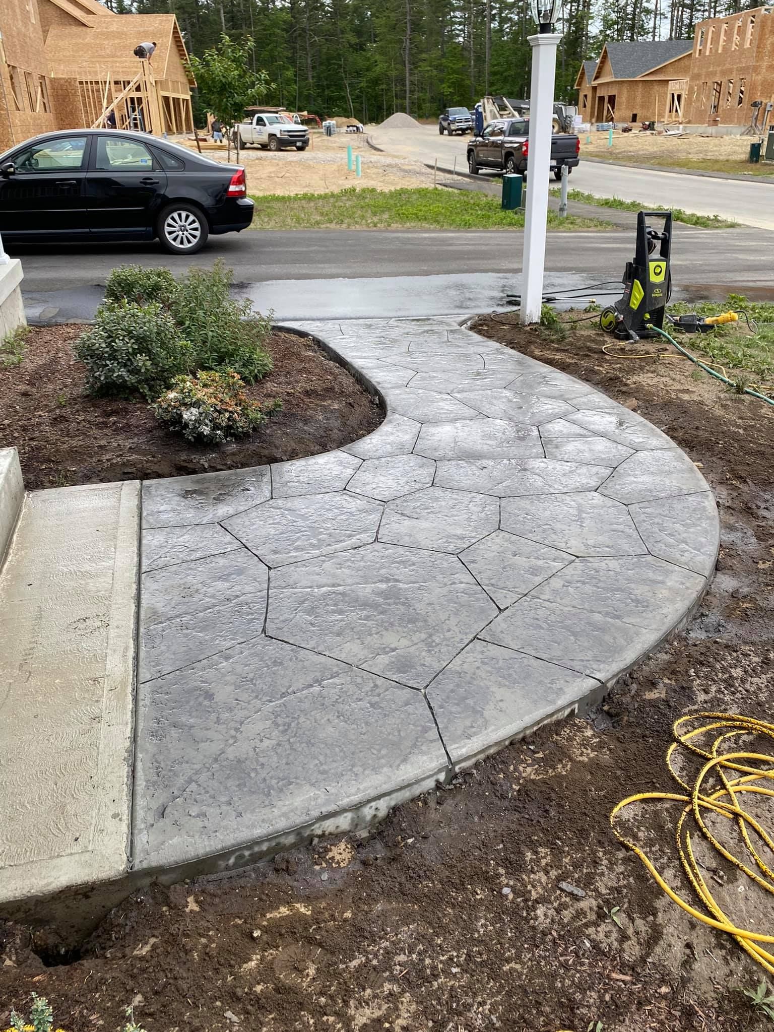 A car is parked on the side of the road next to a concrete walkway.