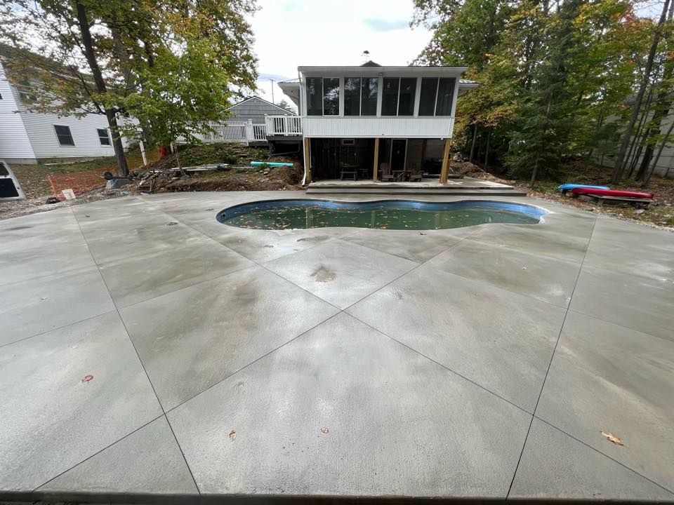 A large concrete patio with a pool in the middle of it and a house in the background.