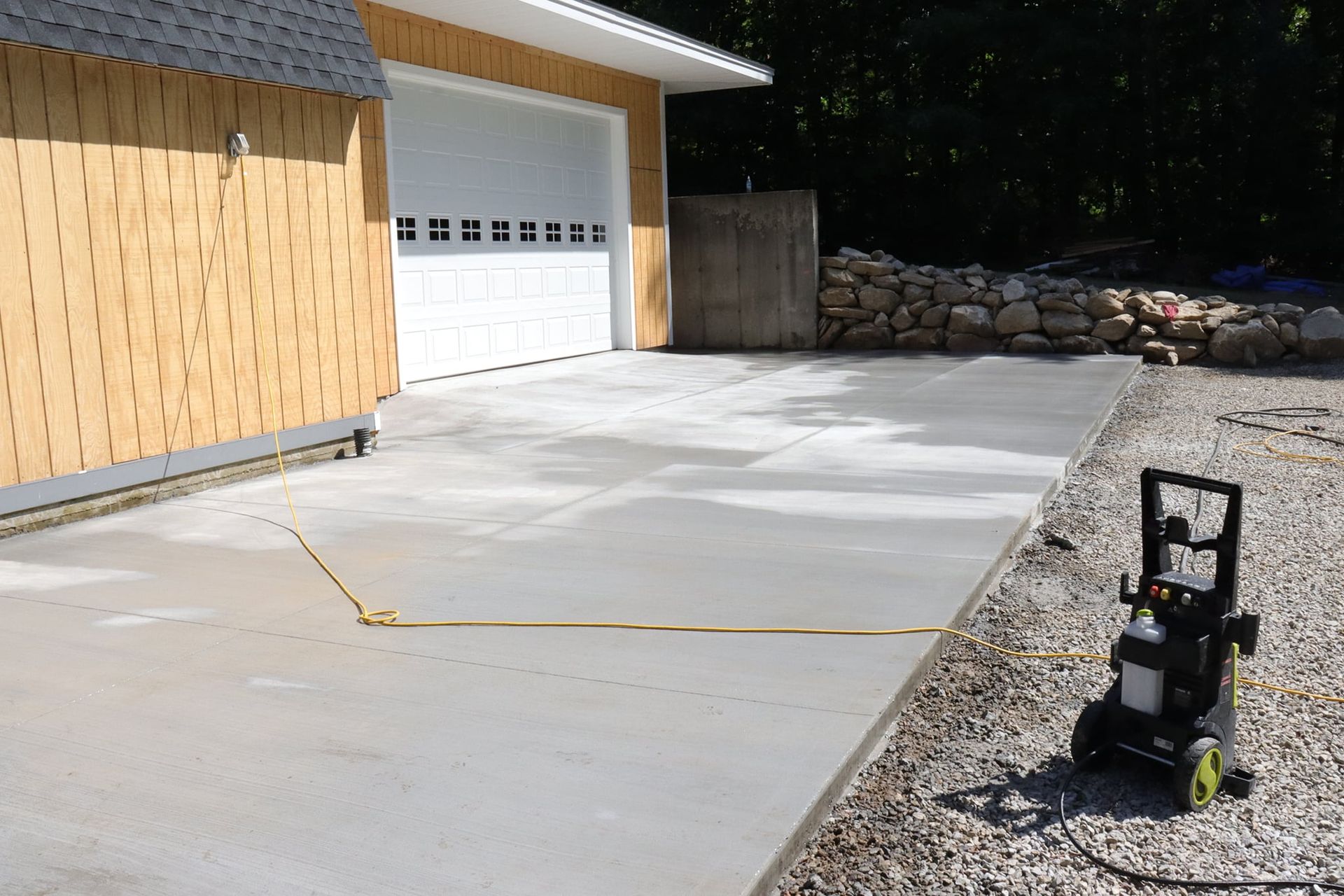 A concrete driveway in front of a garage with a hose attached to it