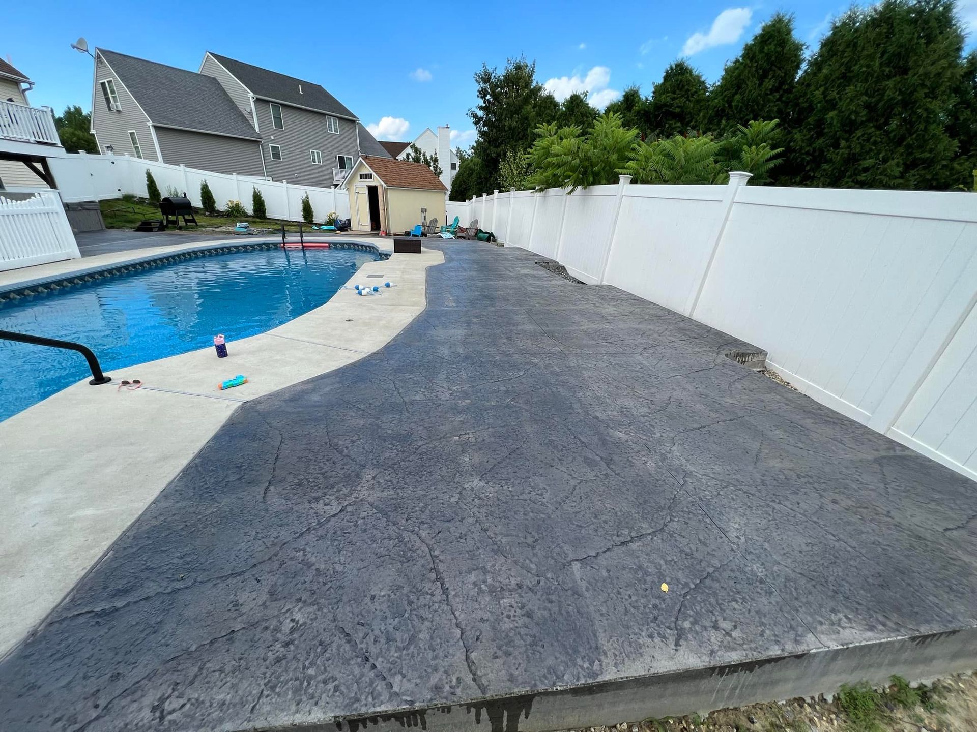 A driveway leading to a swimming pool with a white fence