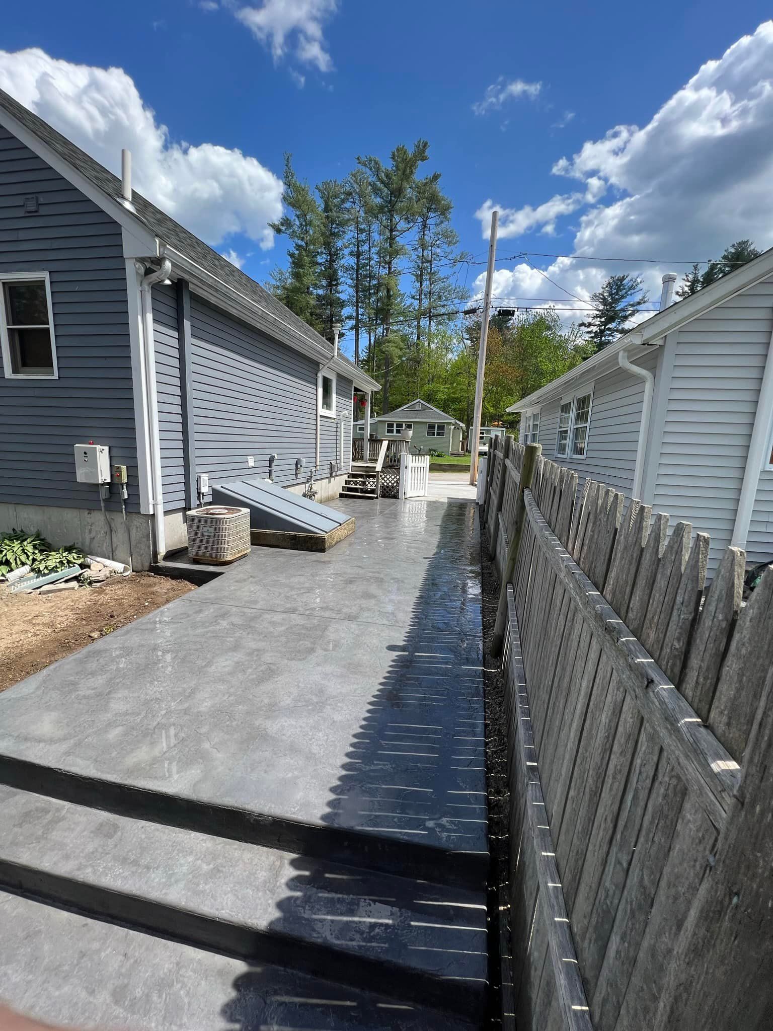 A concrete walkway leading to a house next to a wooden fence.