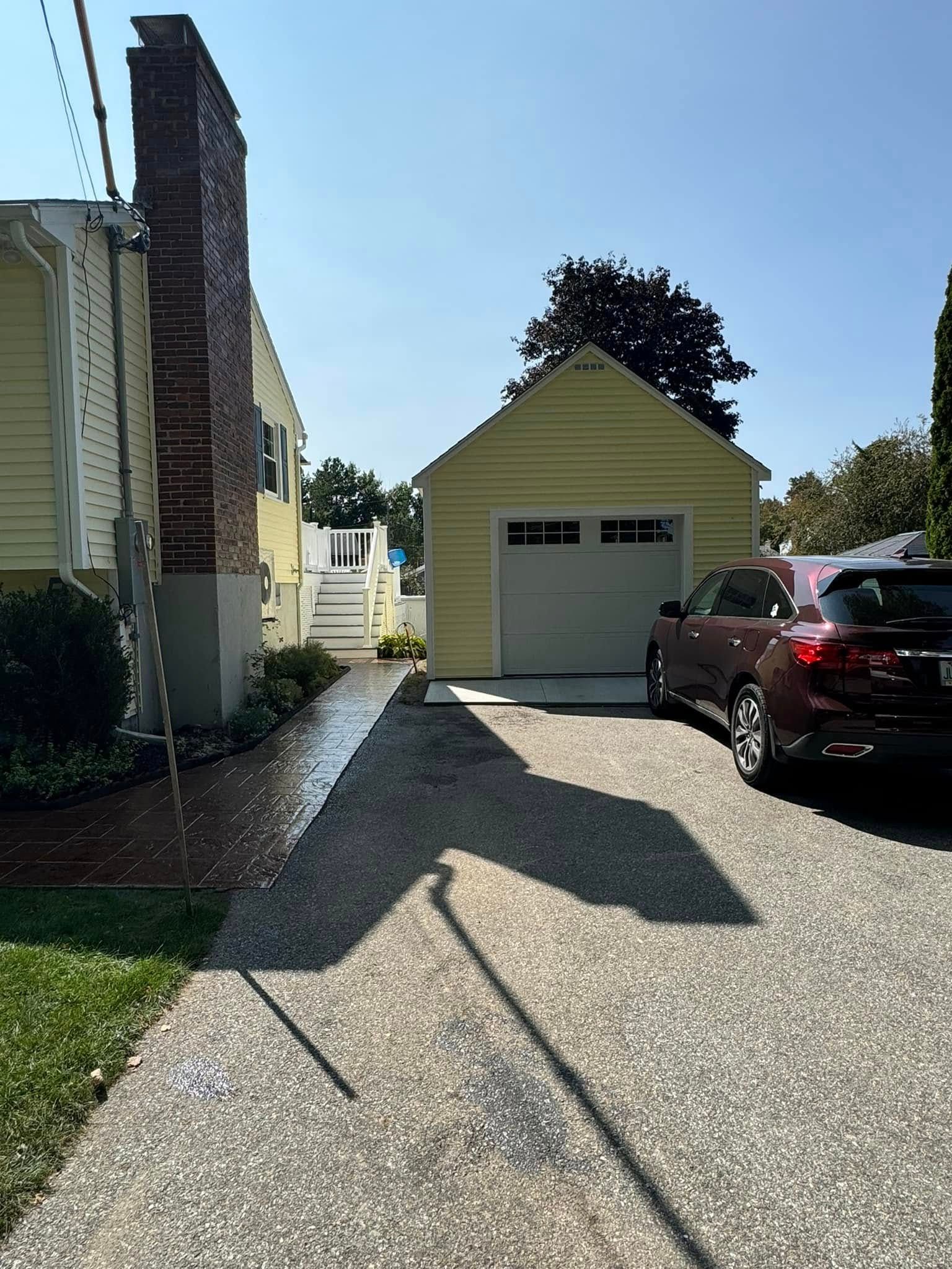 A car is parked in front of a garage next to a house.