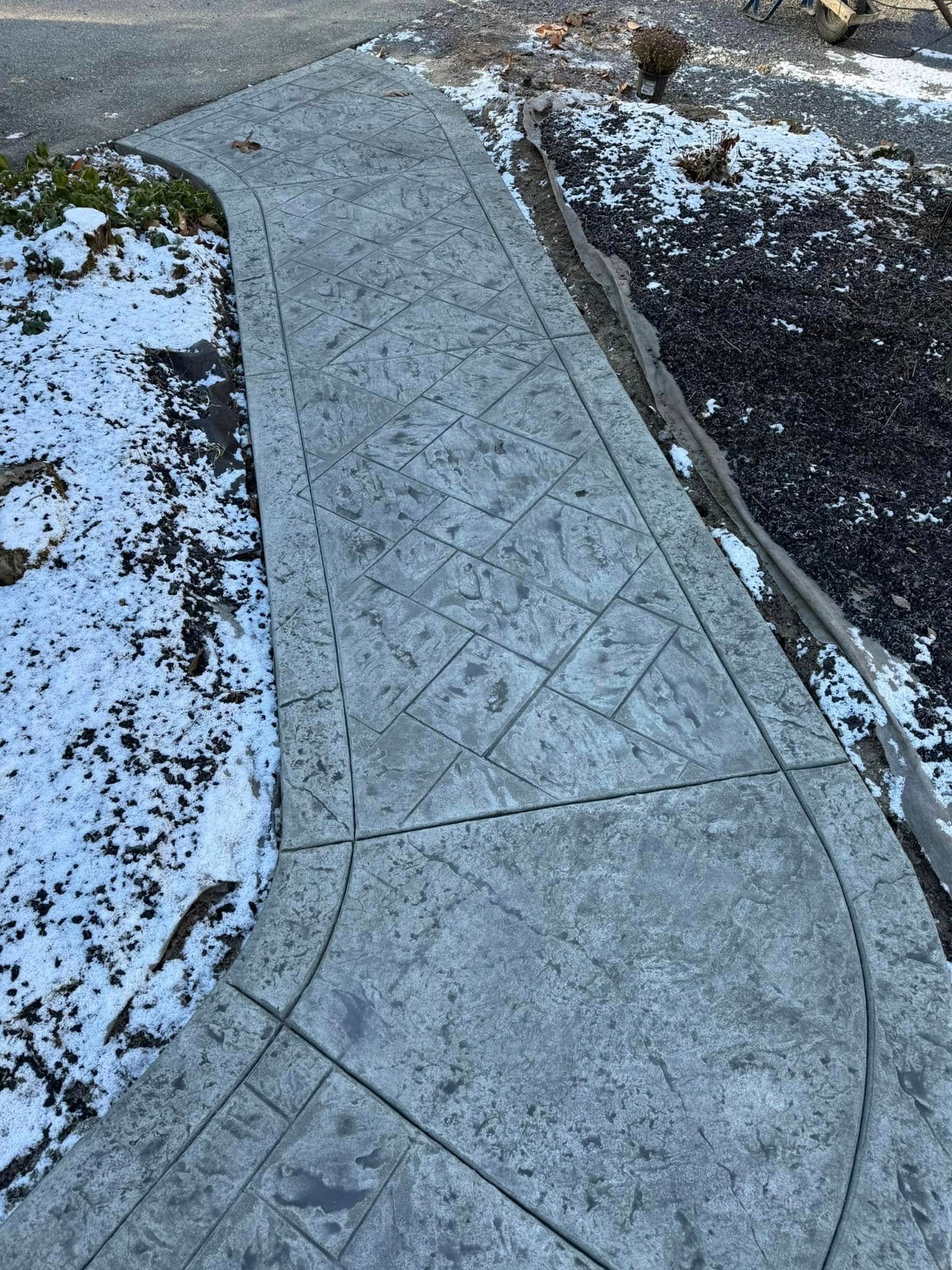 A concrete walkway leading to a garden with snow on the ground.