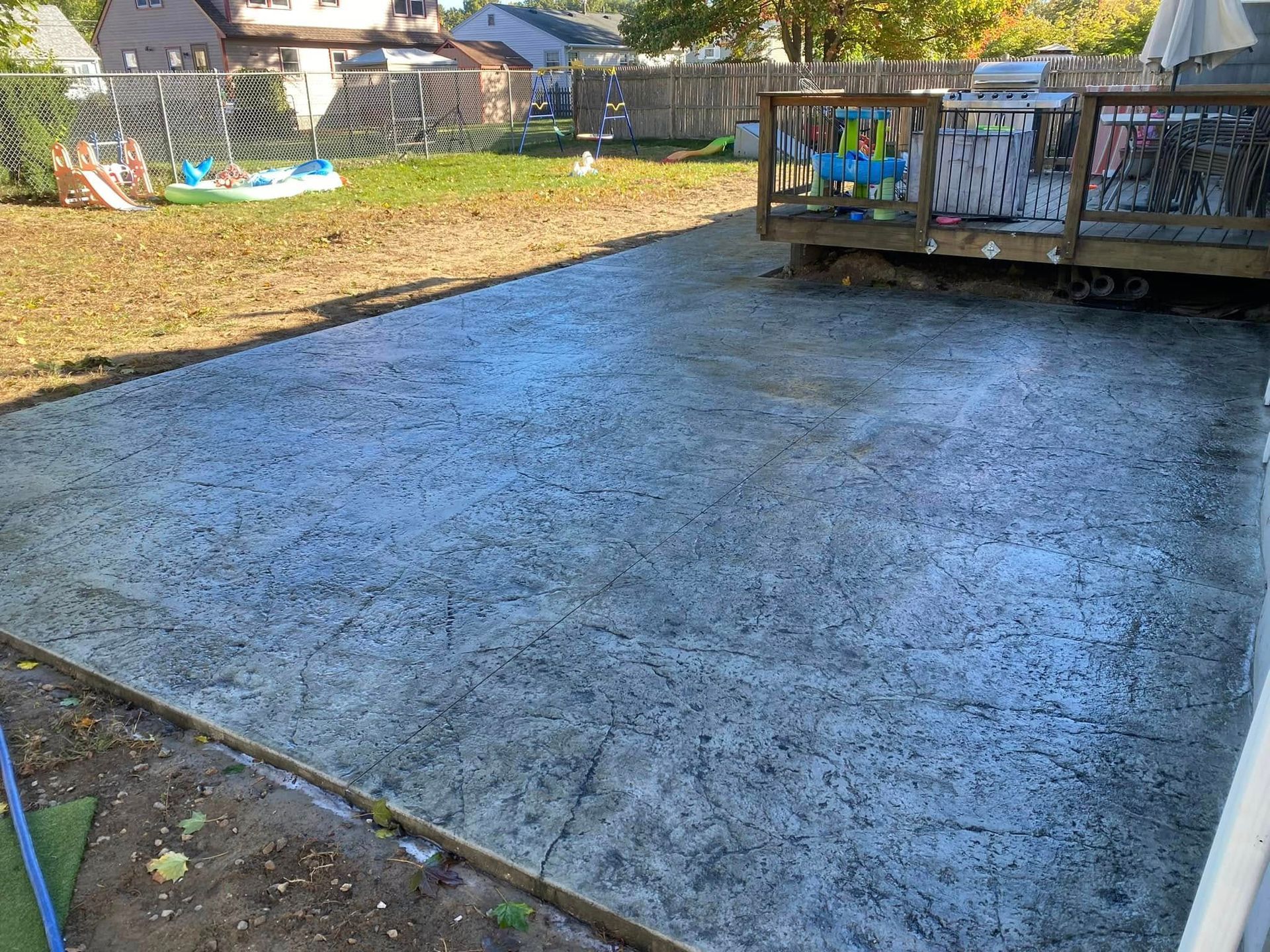 A concrete patio with a wooden deck in the backyard.
